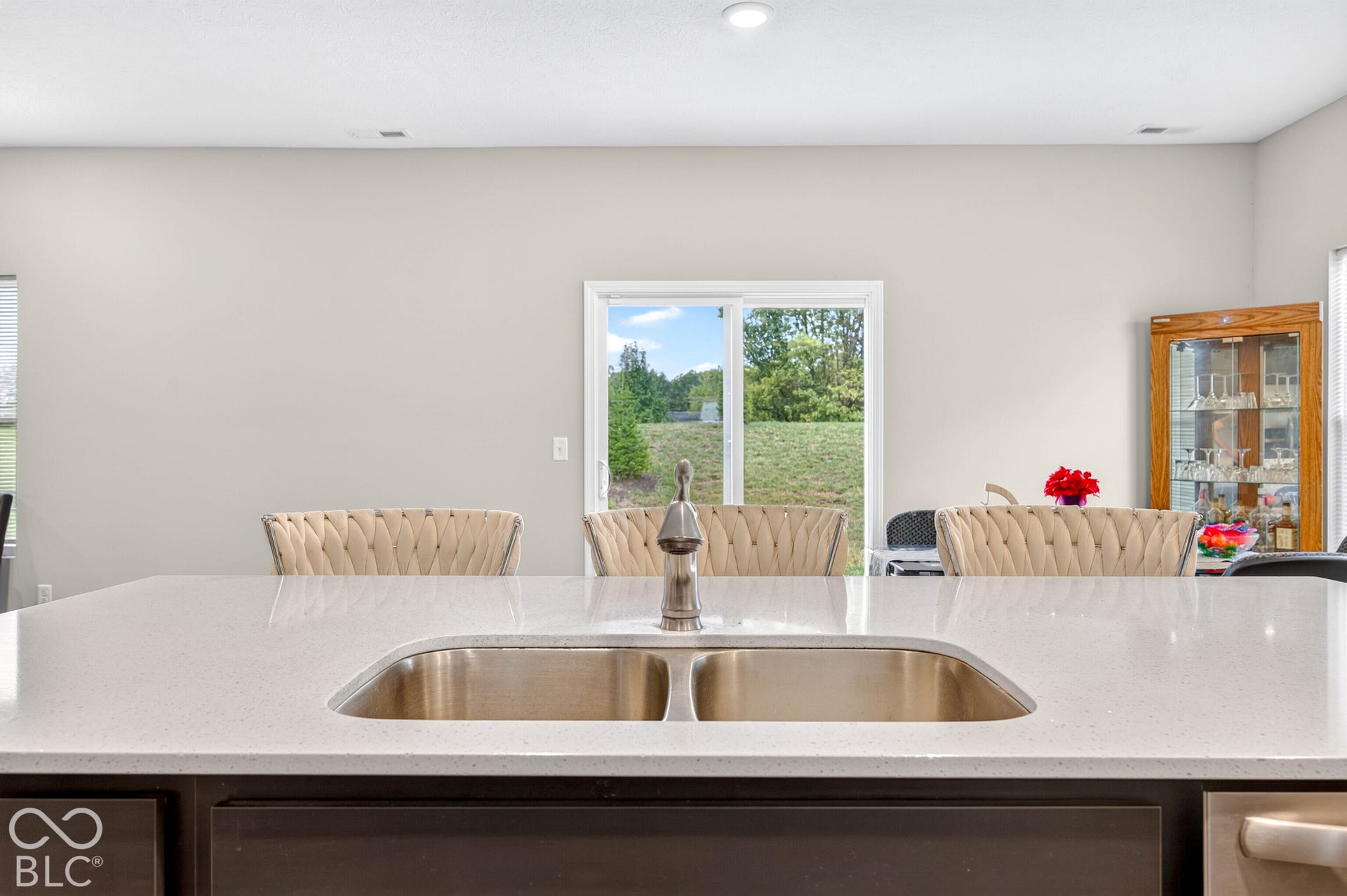Kitchen island featuring a dual-basin stainless steel undermount sink, gooseneck faucet, and solid-surface countertop with sliding glass doors providing outdoor access