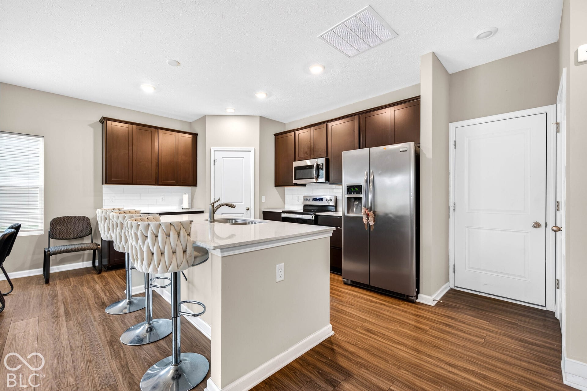 Kitchen featuring dark wood cabinetry, stainless steel appliances, a center island with a stone-finish countertop, and wood-finish flooring