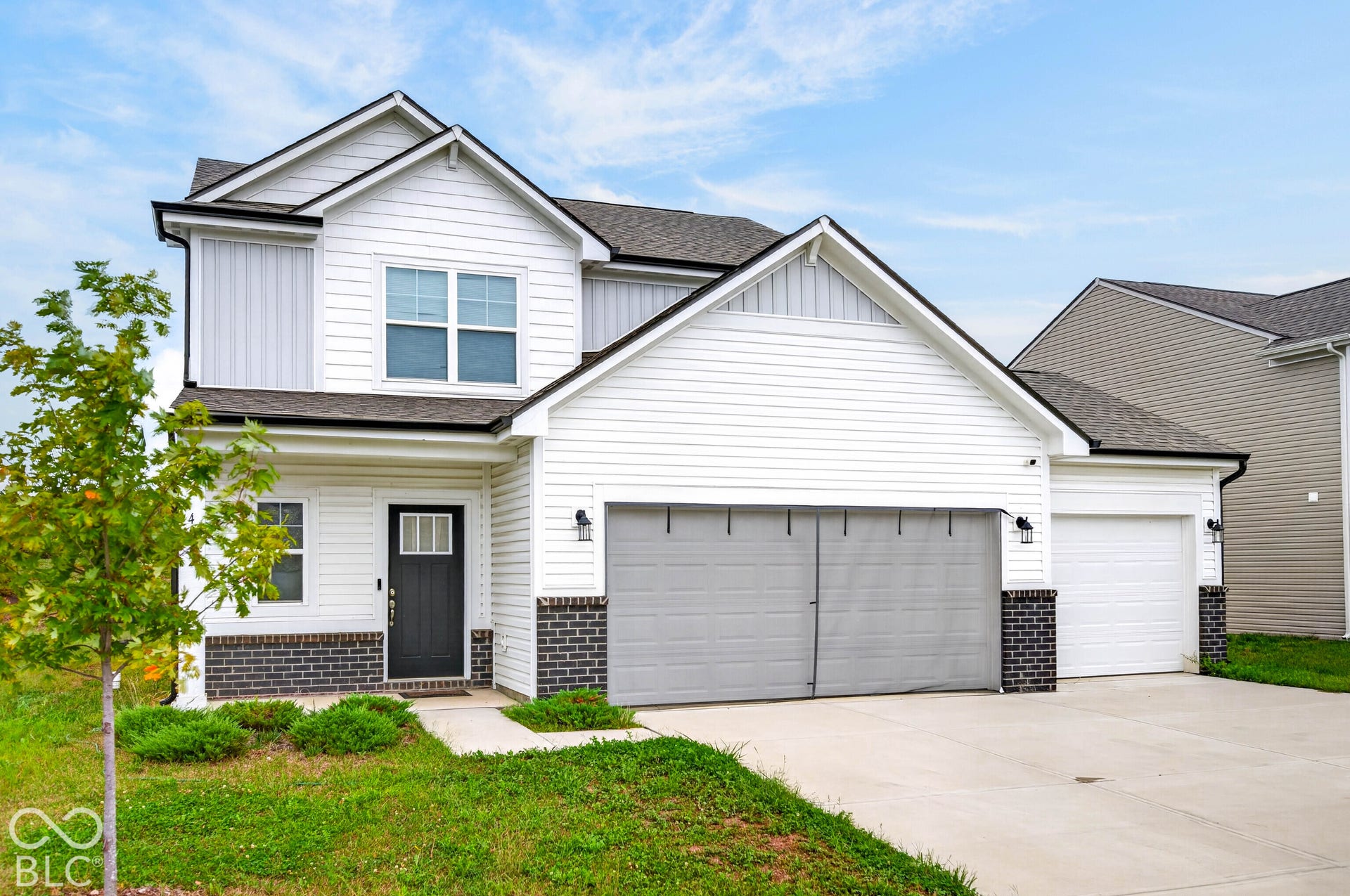 Two-story exterior featuring white horizontal siding, dark brick veneer accents, a multi-gabled roofline, and a three-car garage