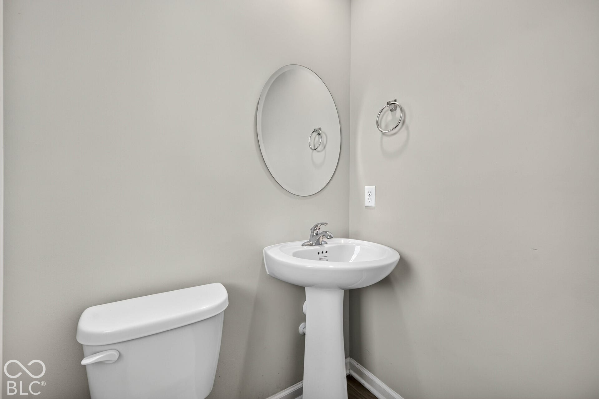 Pedestal sink with a single-handle faucet, circular wall-mounted mirror, and chrome towel ring