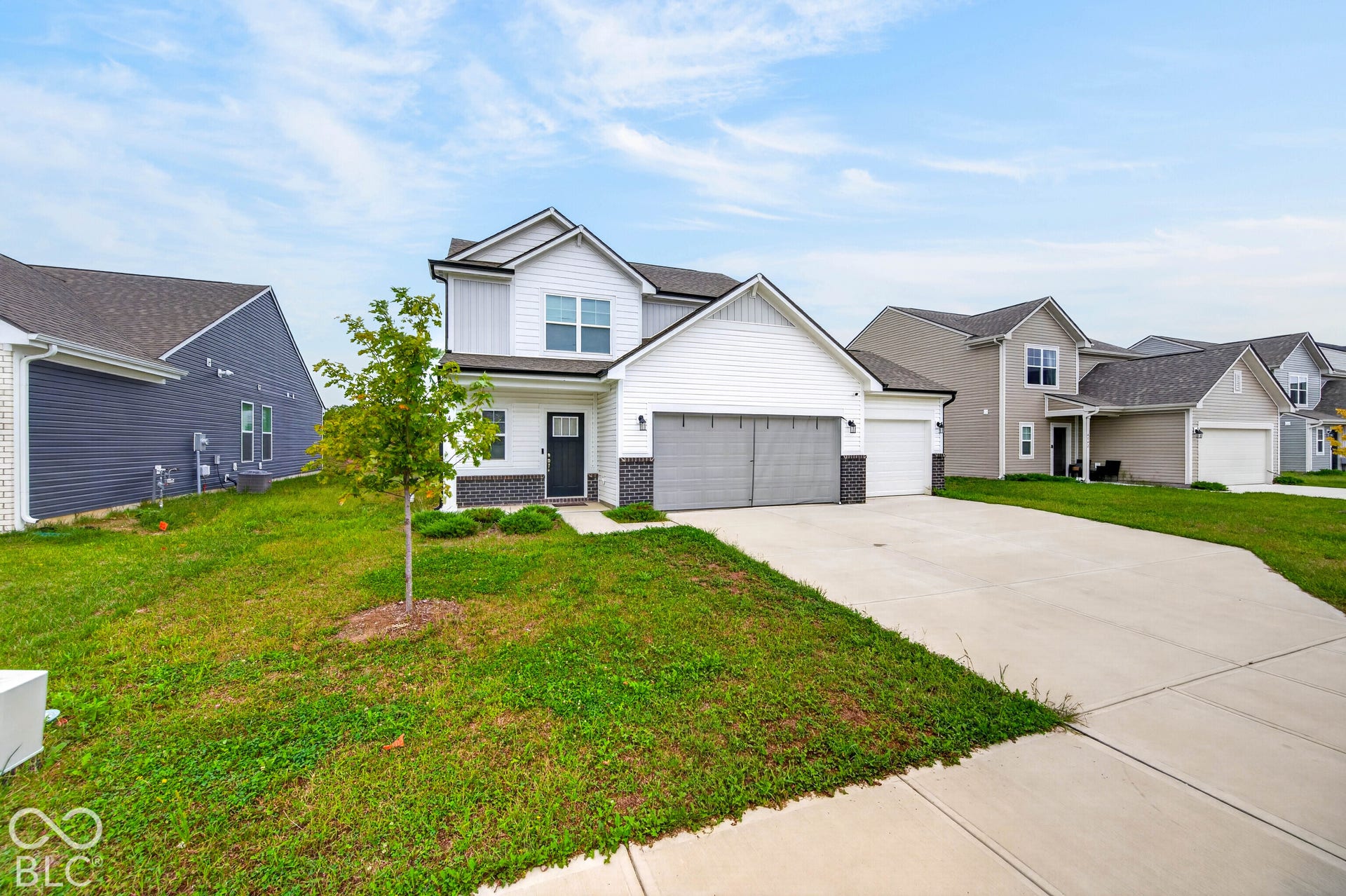 Two-story exterior featuring white horizontal siding, a dark-toned brick masonry base, an attached three-car garage, and a paved concrete driveway