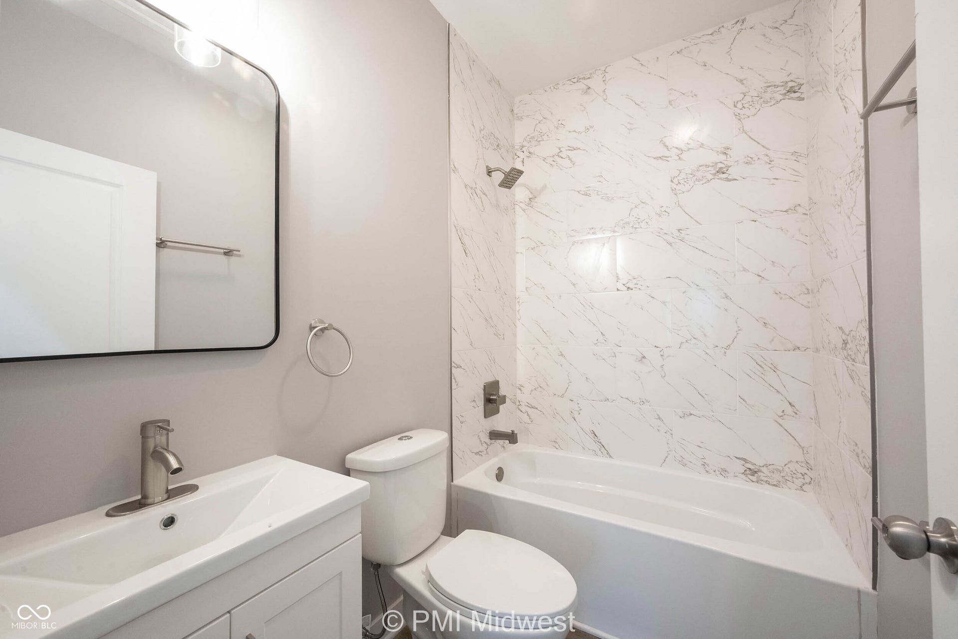 Bathroom featuring a white vanity with an integrated sink and brushed nickel faucet, a rounded rectangular mirror, and a white toilet