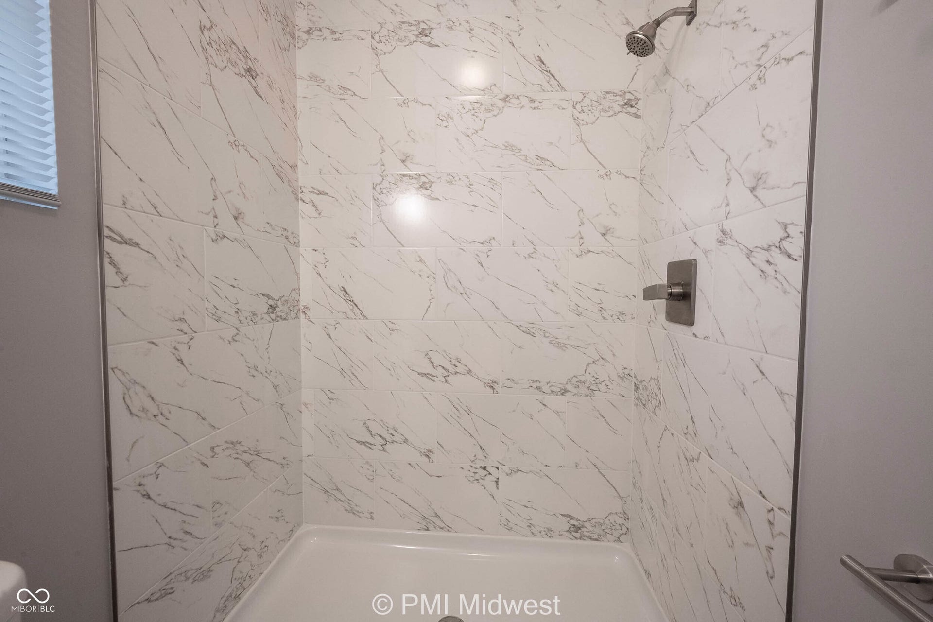 Walk-in shower featuring white marble-look tile walls, a rain-style shower head, and a brushed nickel shower control