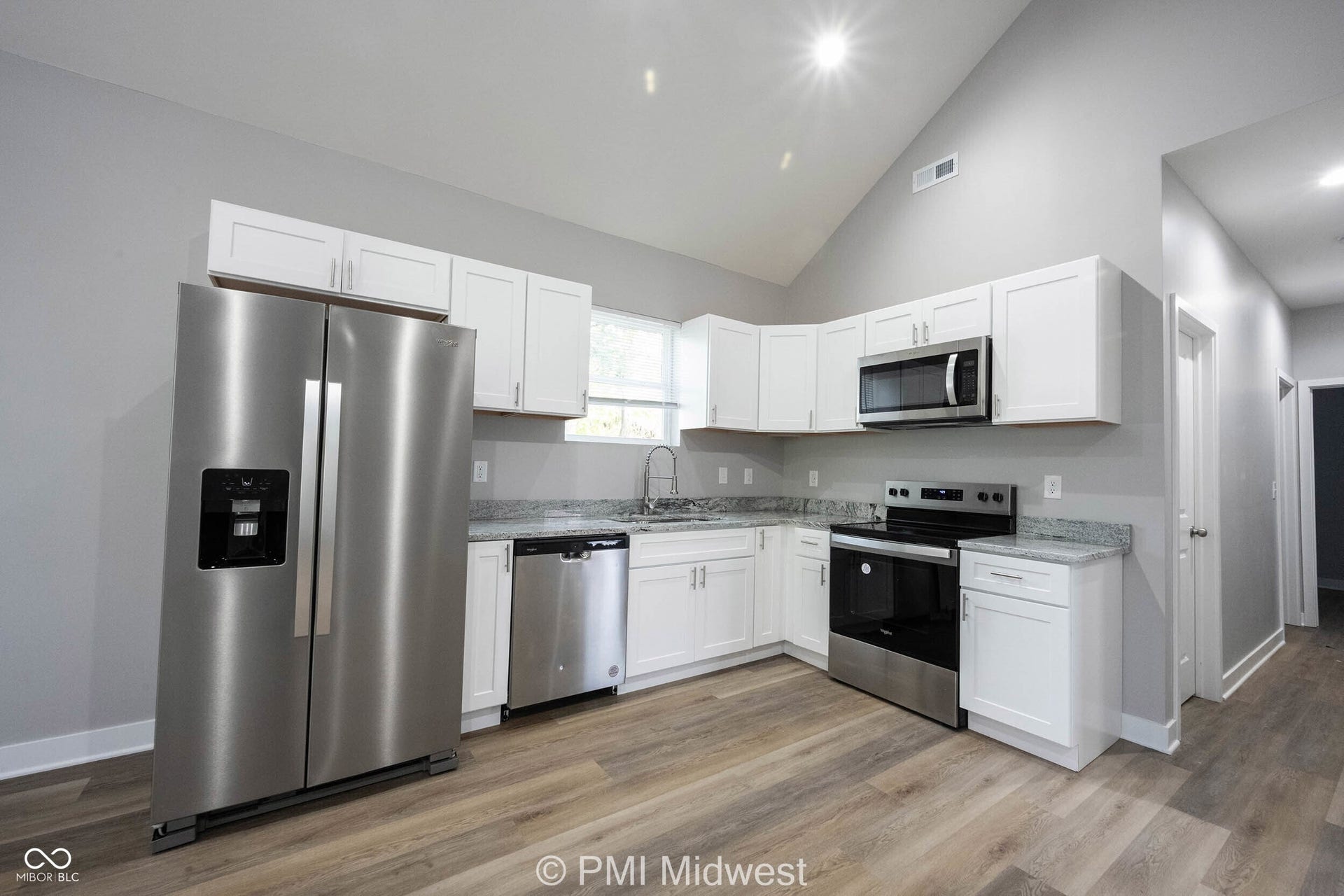 Modern kitchen featuring white cabinetry, stainless steel appliances, light-toned wood-finish flooring, a vaulted ceiling, and granite-style countertops