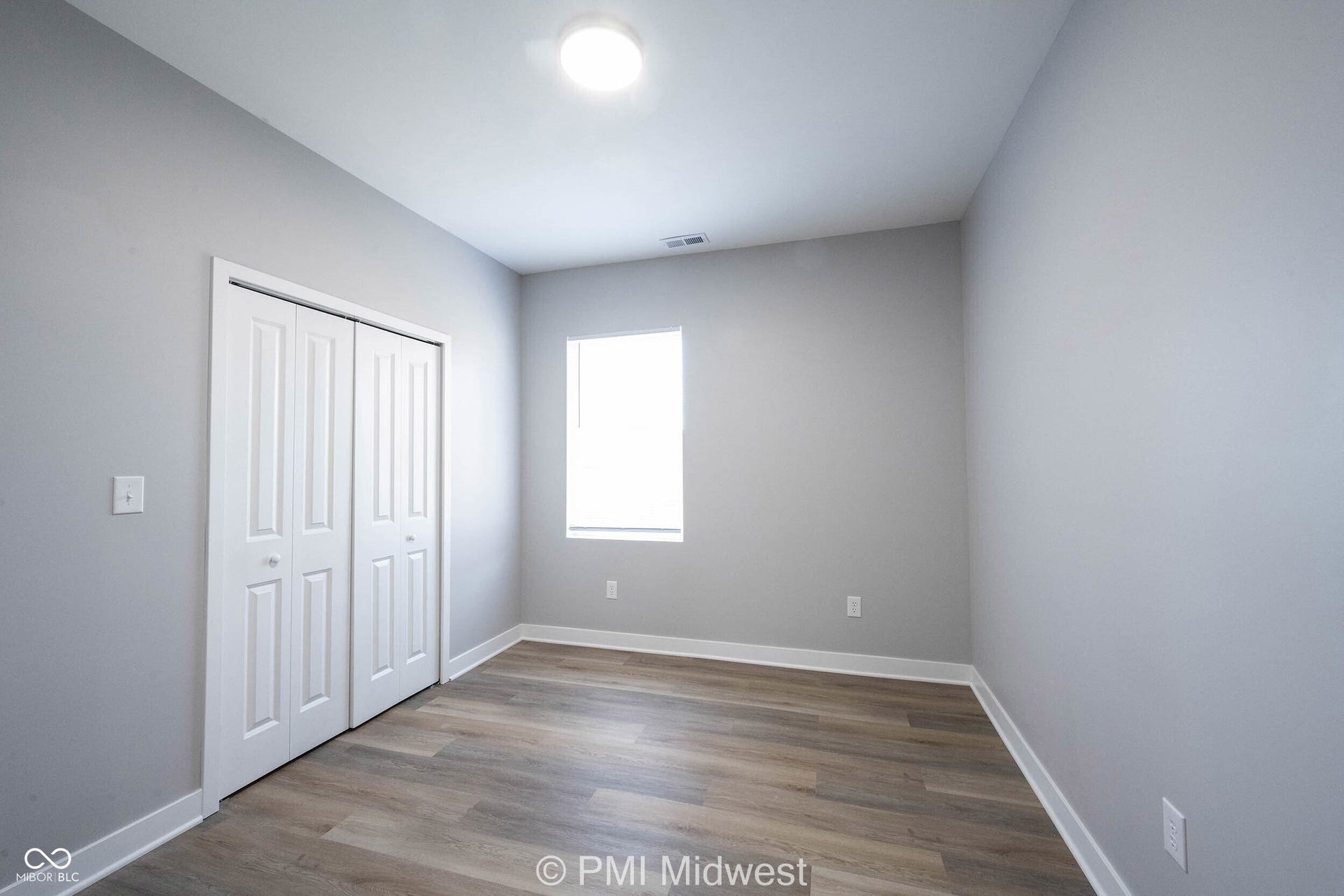 Room featuring wood-finish flooring, light gray walls, a window with natural light, a bi-fold closet, and ceiling lighting