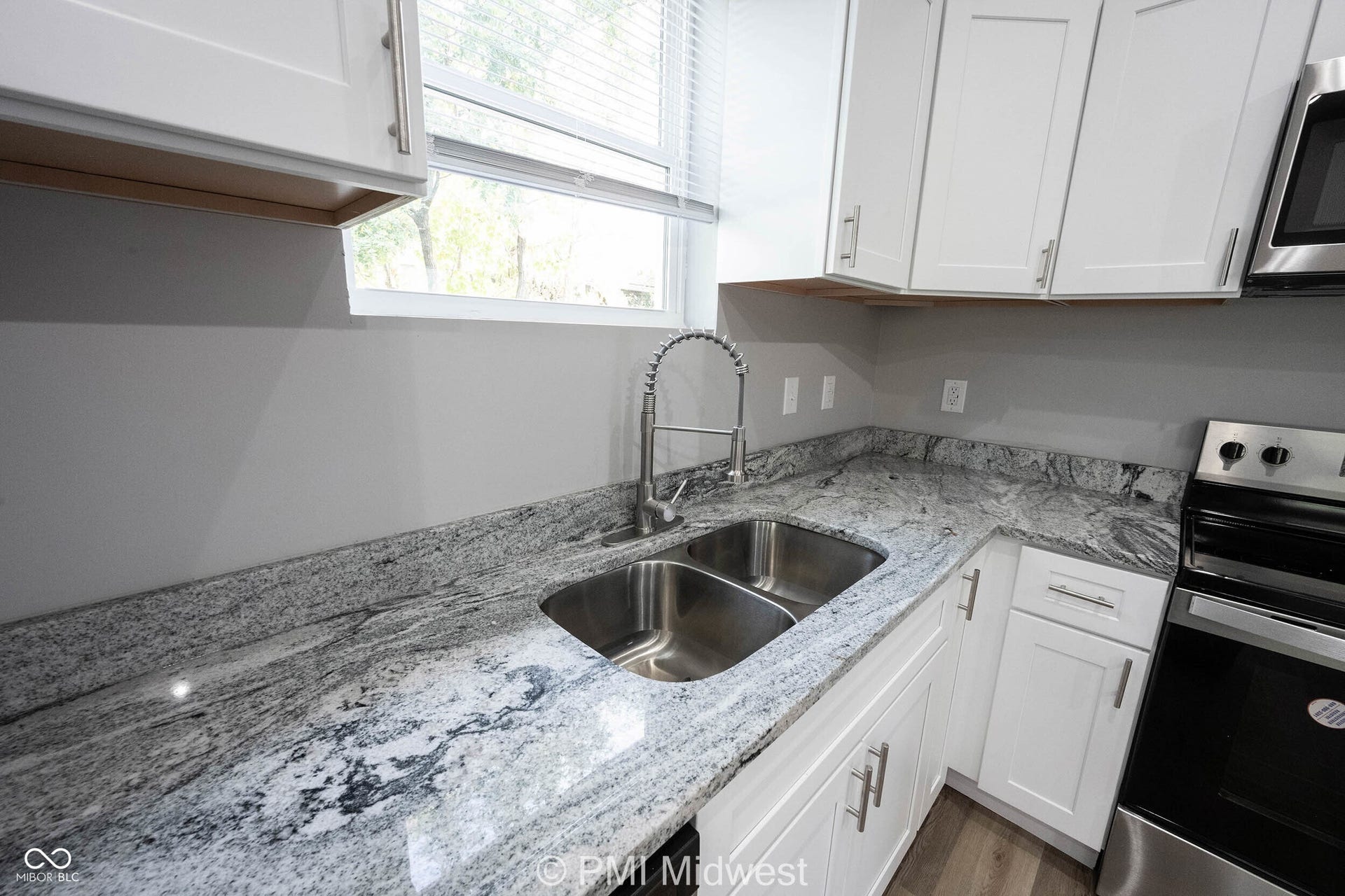 Kitchen featuring white shaker-style cabinetry, granite countertops, a stainless steel double-basin sink with a gooseneck faucet, and stainless steel appliances