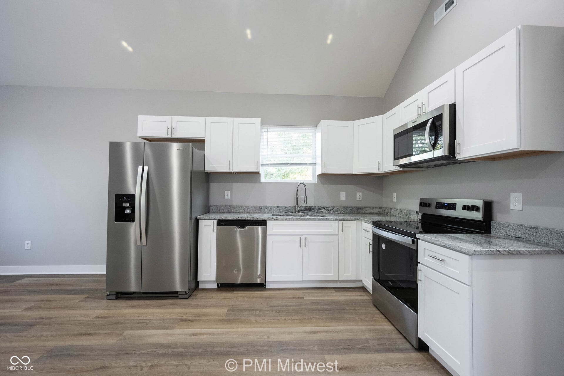 Kitchen featuring white shaker cabinetry, stainless steel appliances, speckled stone countertops, wood-finish flooring, and a vaulted ceiling
