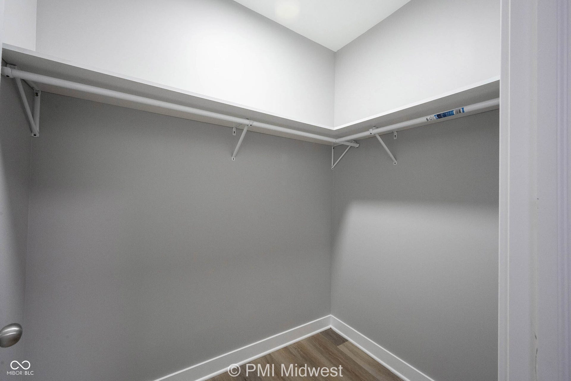 Corner walk-in closet featuring light gray walls, white baseboards, and wood-finish flooring