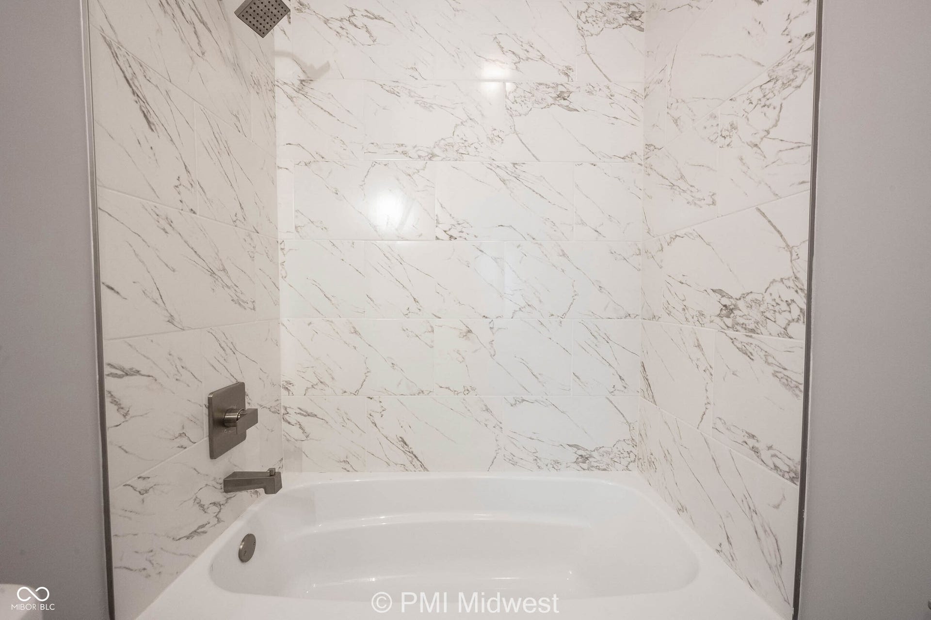 Bathtub with white marble-look tile surround, brushed nickel fixtures, and a rain shower head