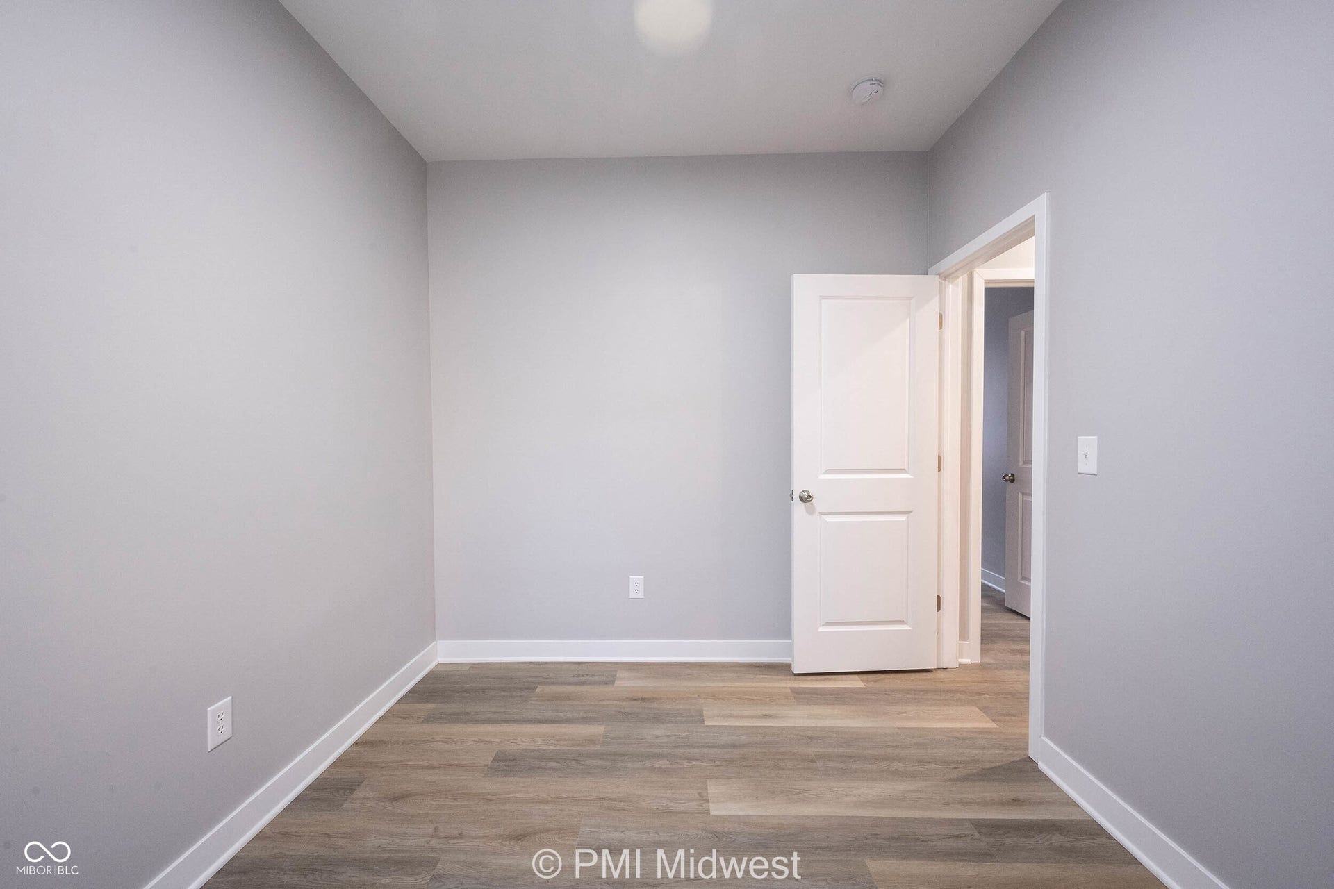 Room featuring light grey walls, wood-finish flooring, white baseboards, and a contemporary two-panel interior door with brushed nickel hardware