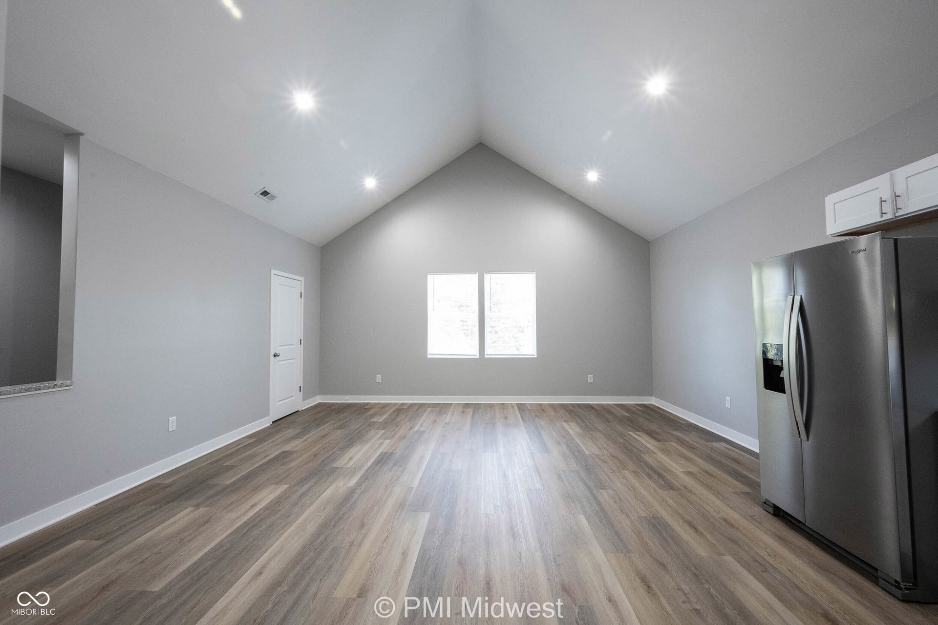 Spacious room featuring a vaulted ceiling with recessed lighting, wood-finish flooring, and white baseboards