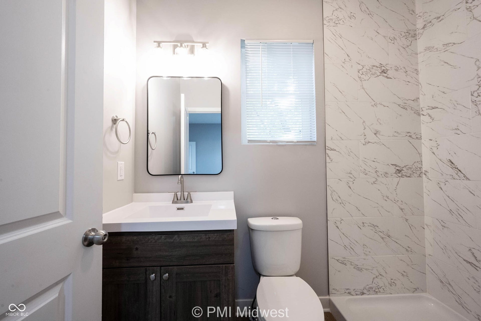 Bathroom featuring a wood-finish vanity with a white countertop and integrated sink, a rectangular framed mirror, and a track light fixture