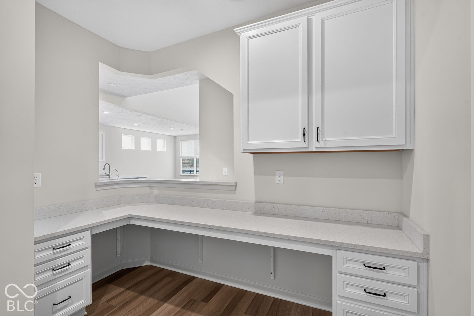 Built-in L-shaped desk featuring white cabinetry, stone-finish countertops, matte black hardware, and wood-finish flooring