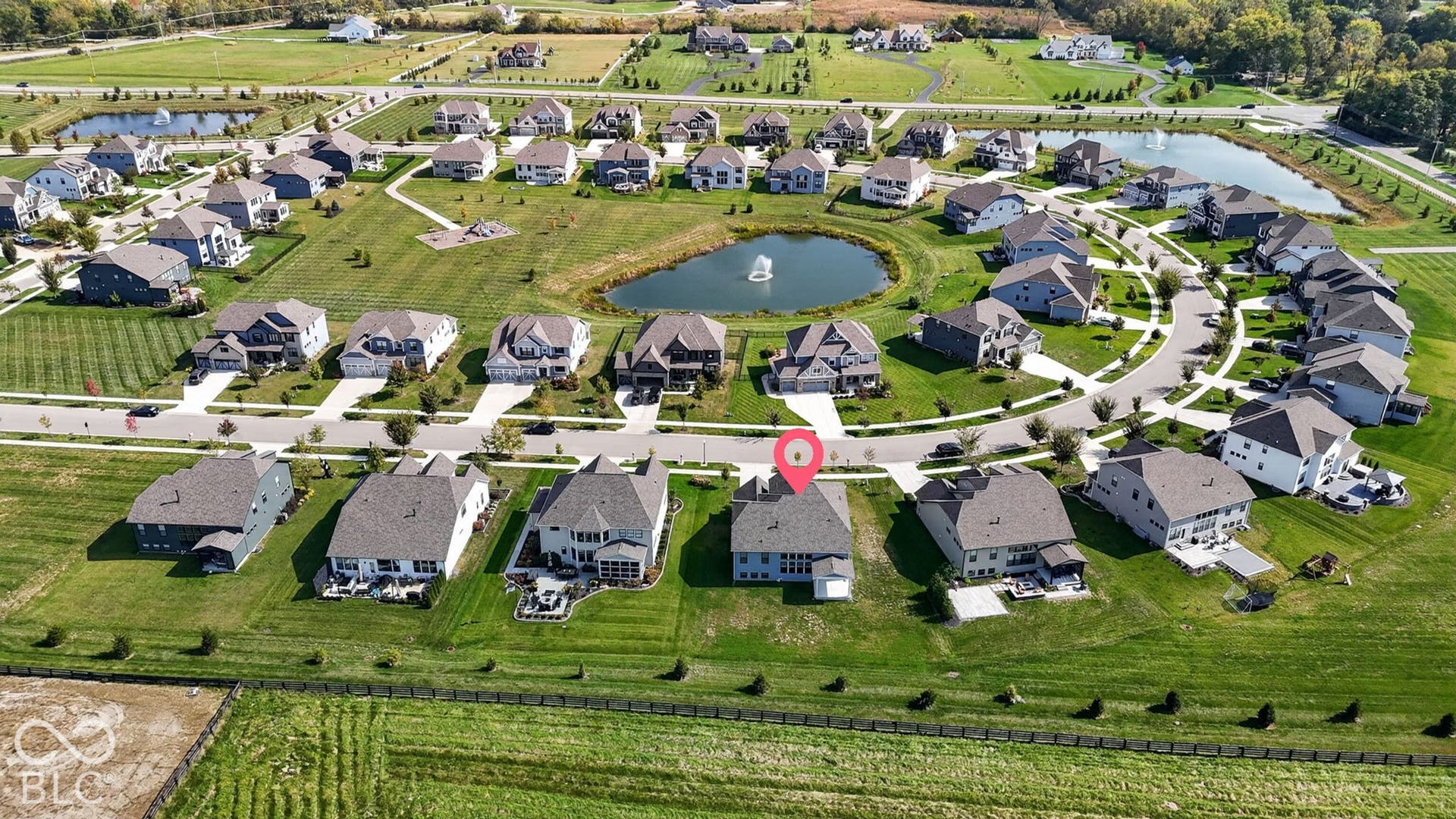 Aerial perspective of a residential community featuring a central pond with a fountain, paved cul-de-sac streets, manicured green spaces, and dense perimeter landscaping