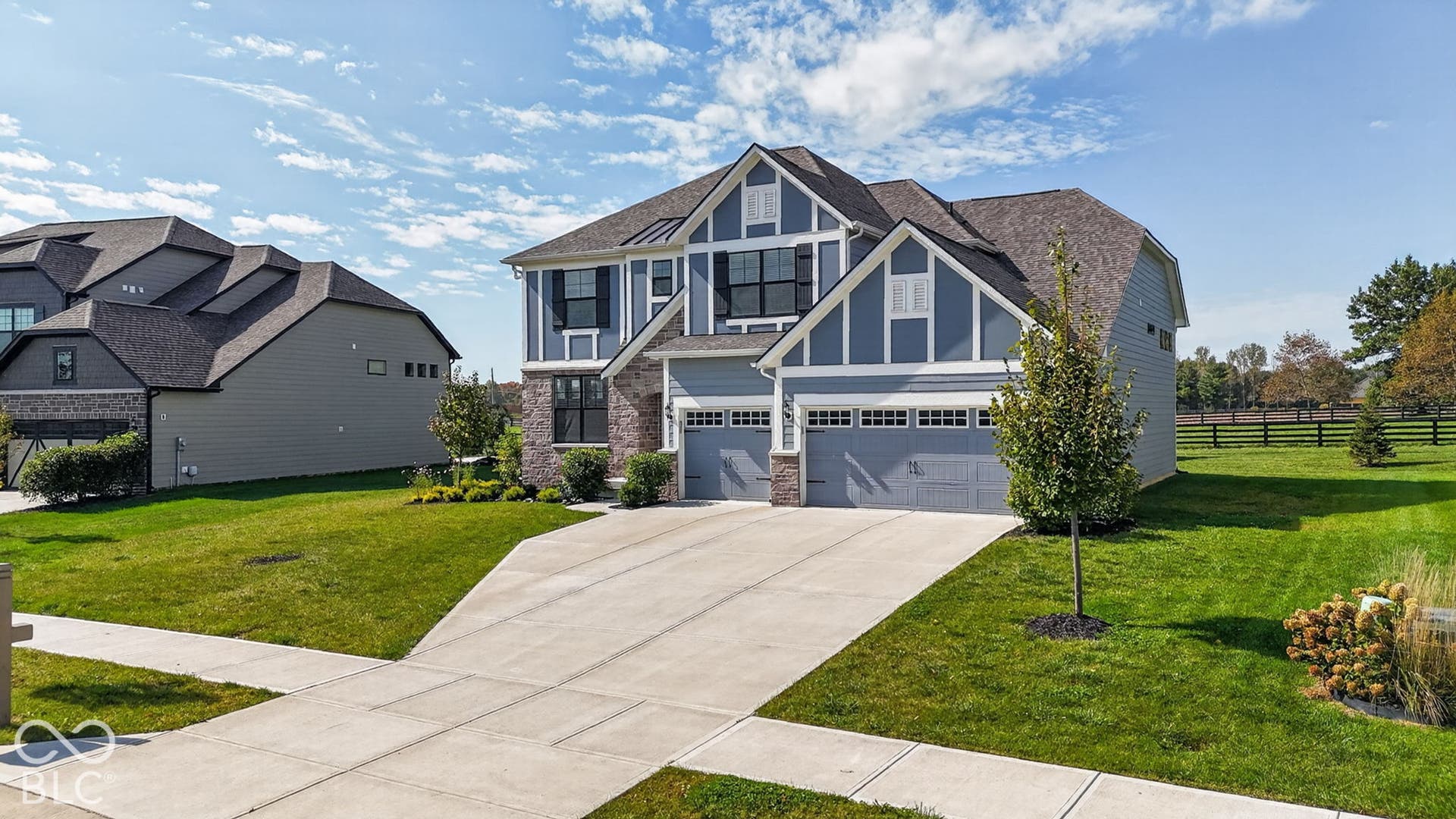 Two-story residence featuring blue horizontal siding, decorative gable truss detailing, stone veneer accents, an asphalt shingle roof, and a three-car garage