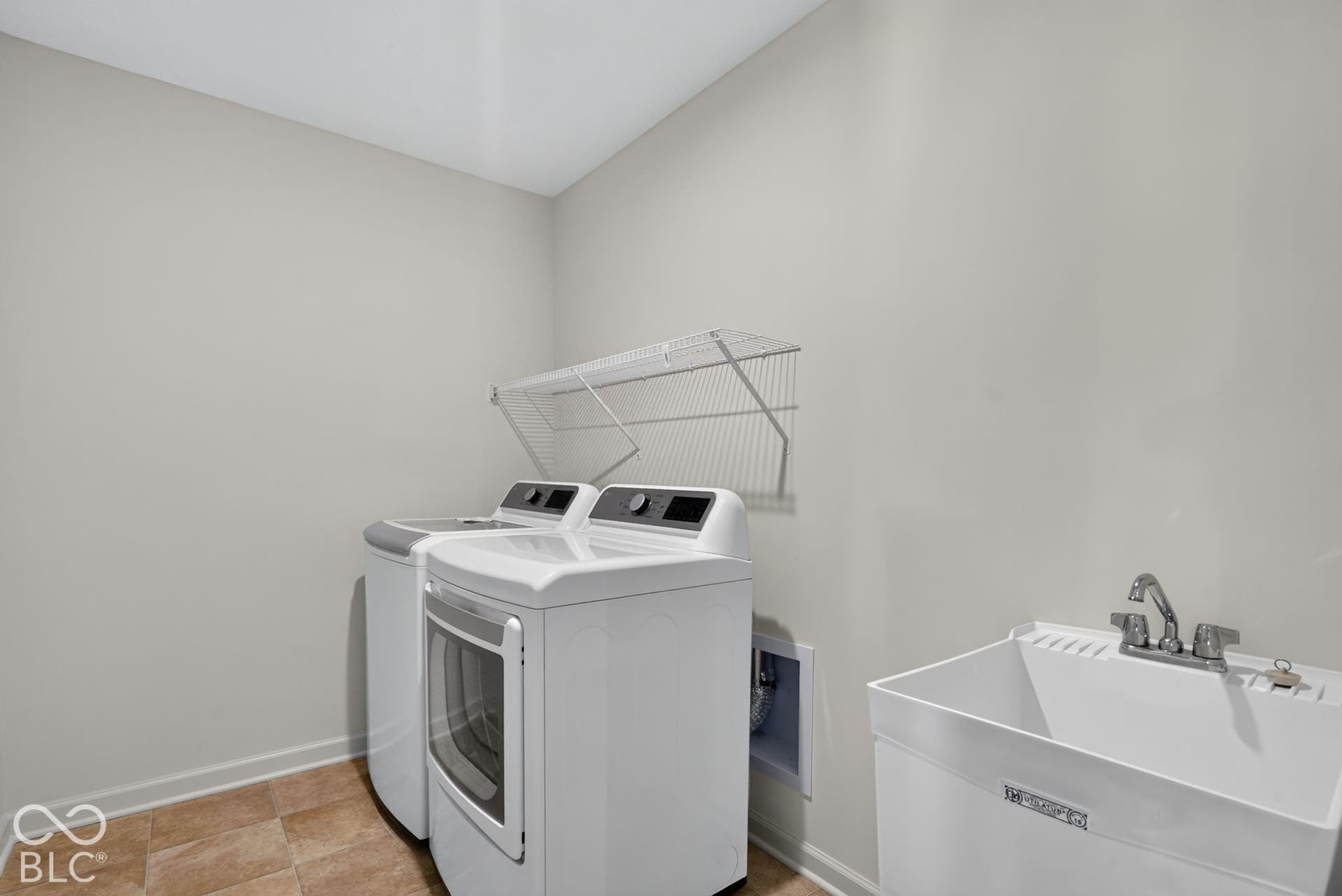 Utility space featuring ceramic tile flooring, a deep basin sink with a dual-handle faucet, and wall-mounted wire shelving