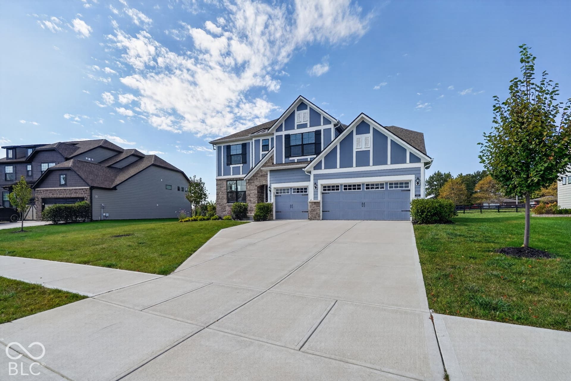 Two-story residence featuring blue horizontal siding with white trim, stone veneer accents, a three-car garage, and a concrete driveway
