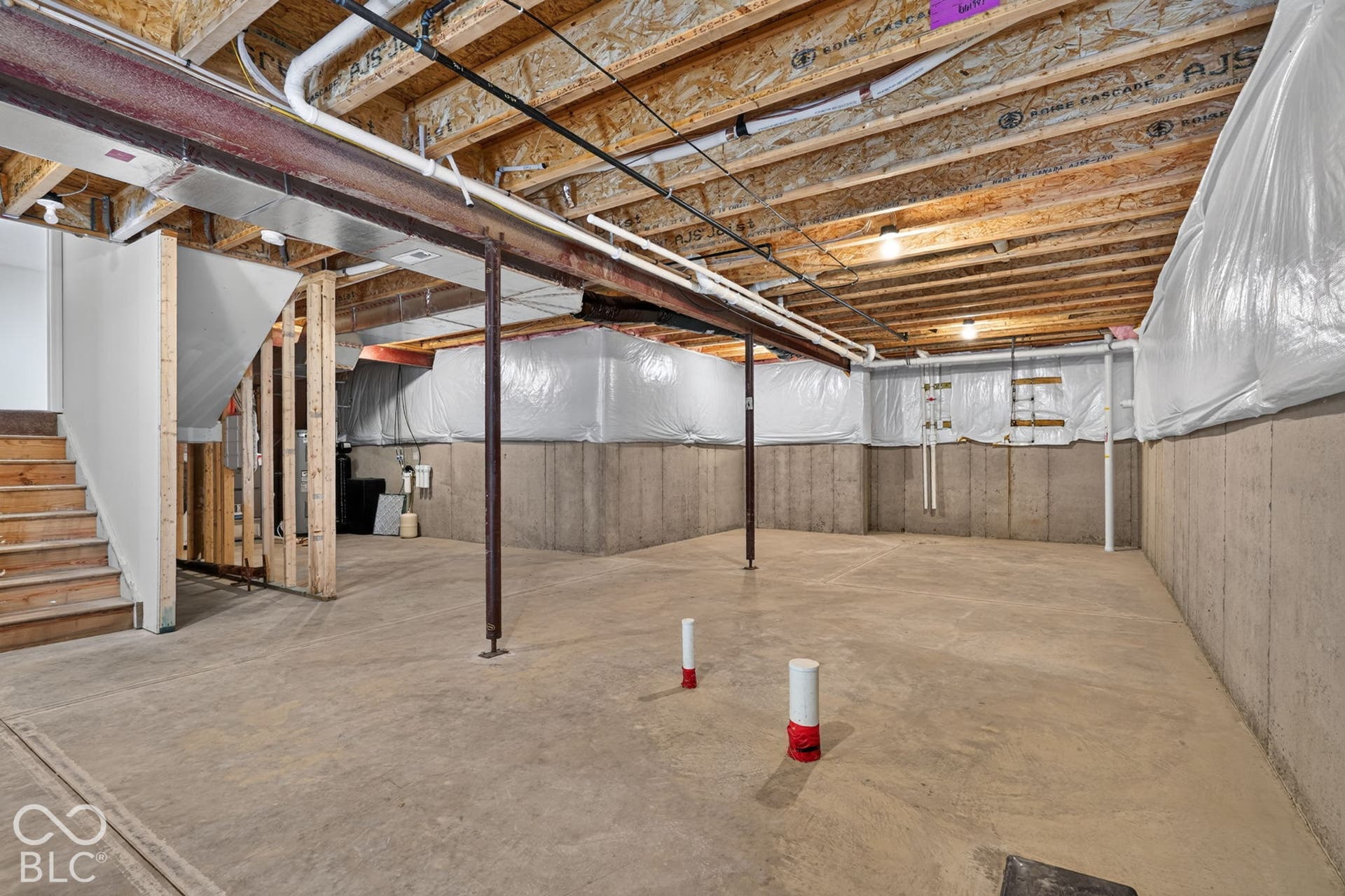 Unfinished lower level featuring poured concrete walls, exposed wood ceiling joists, concrete flooring, and structural steel support columns