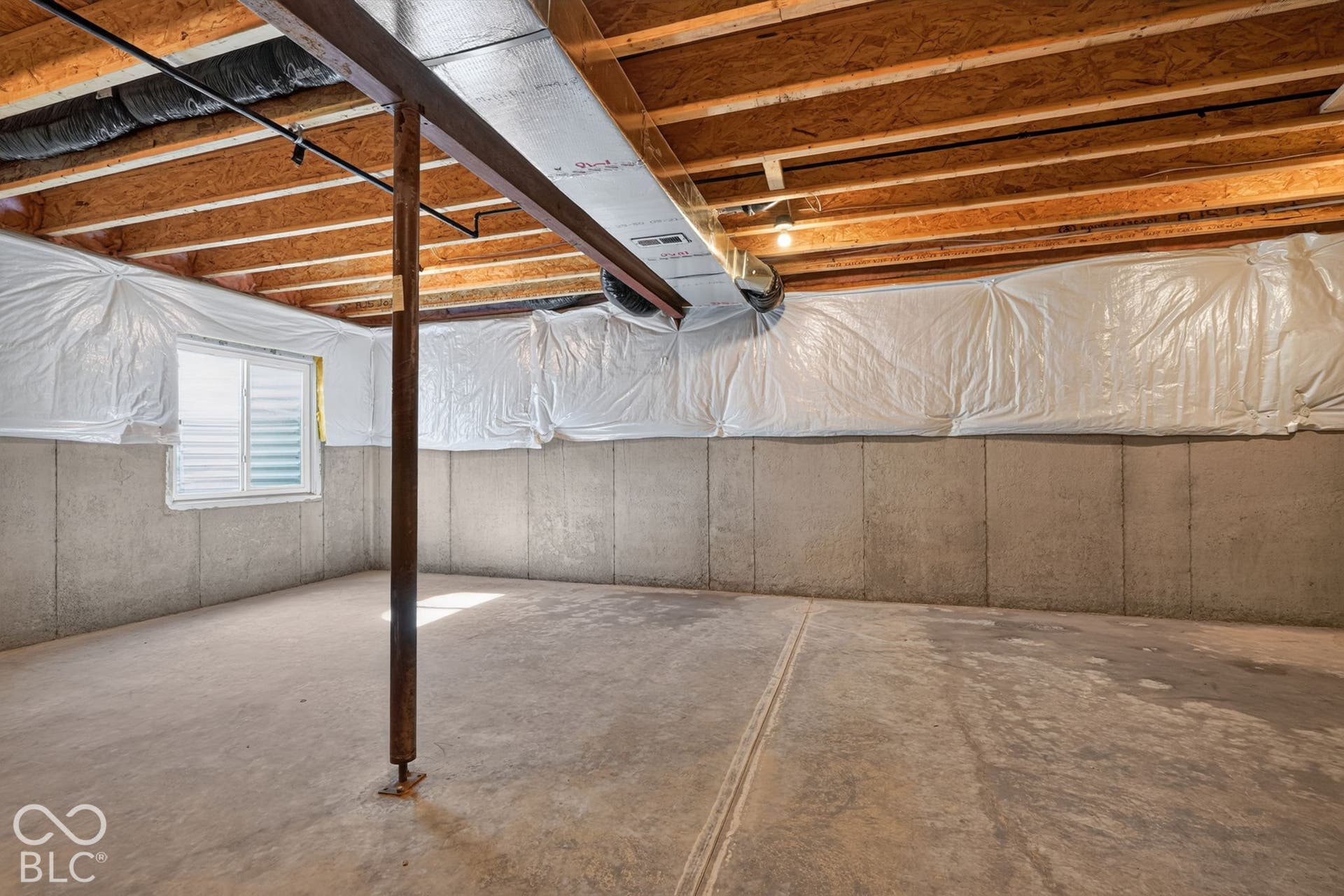 Unfinished lower level featuring concrete foundation walls, exposed wooden joists, a single metal support column, and a window