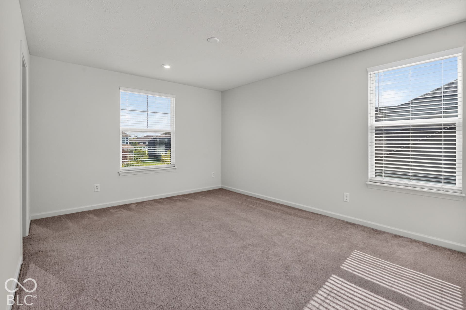 Neutral-toned room featuring neutral carpeting, recessed ceiling lighting, and two windows with installed horizontal blinds