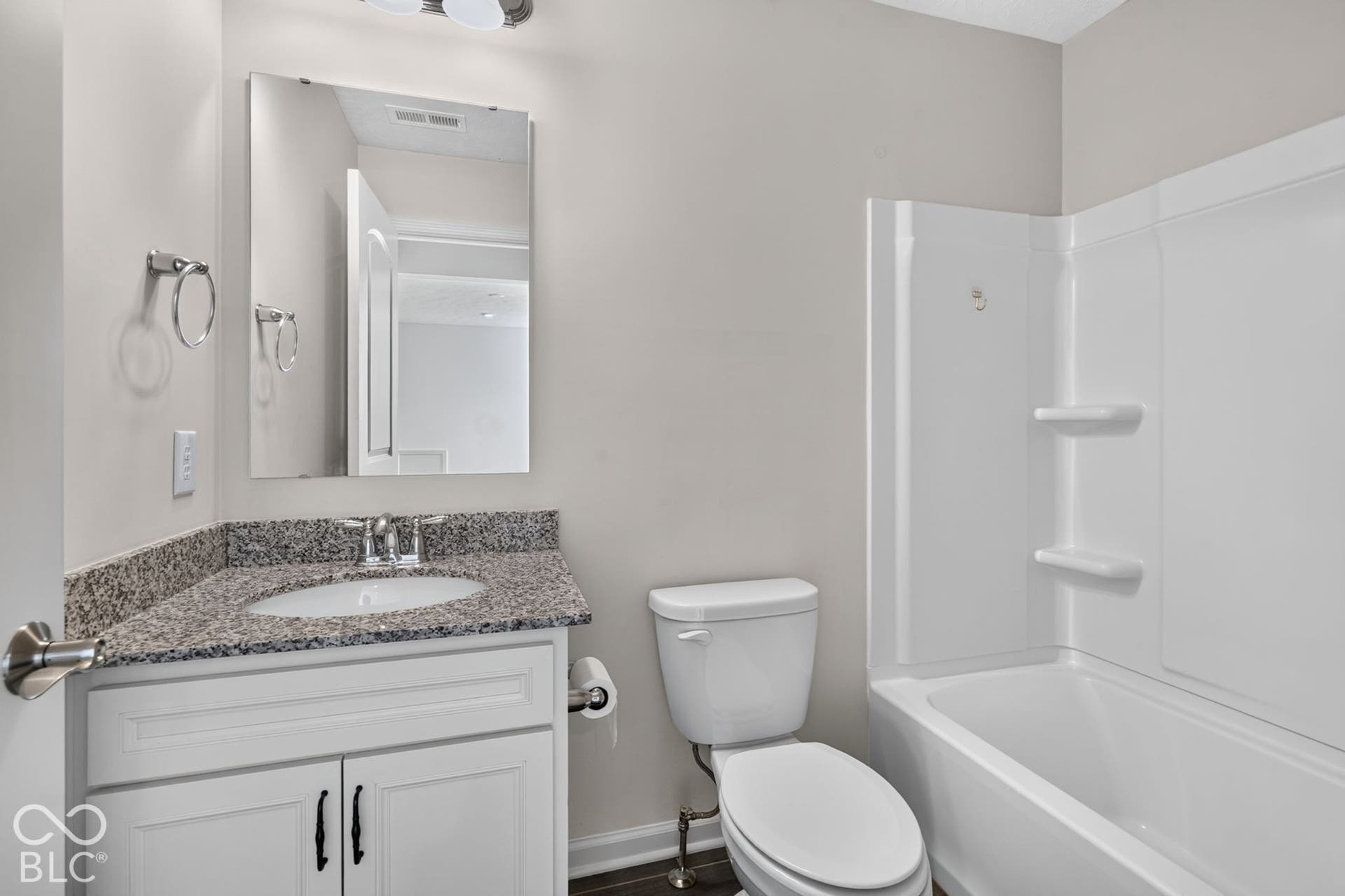 Bathroom featuring a white vanity cabinet with stone-finish countertop, integrated sink, polished chrome faucet, rectangular frameless mirror, and a white acrylic tub-shower combination