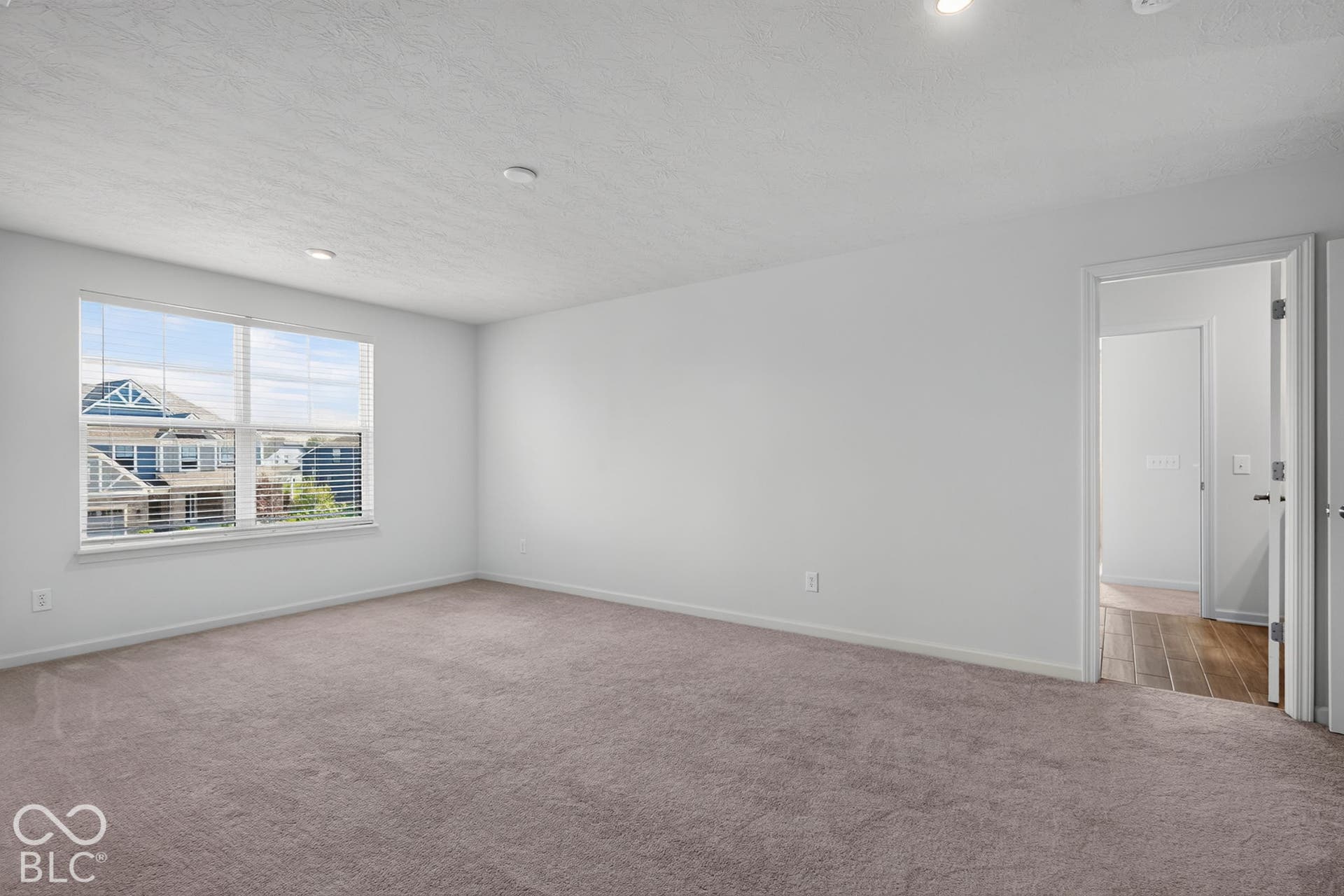 Neutral-toned wall-to-wall carpeting, recessed ceiling lighting, and a dual-pane window with white trim