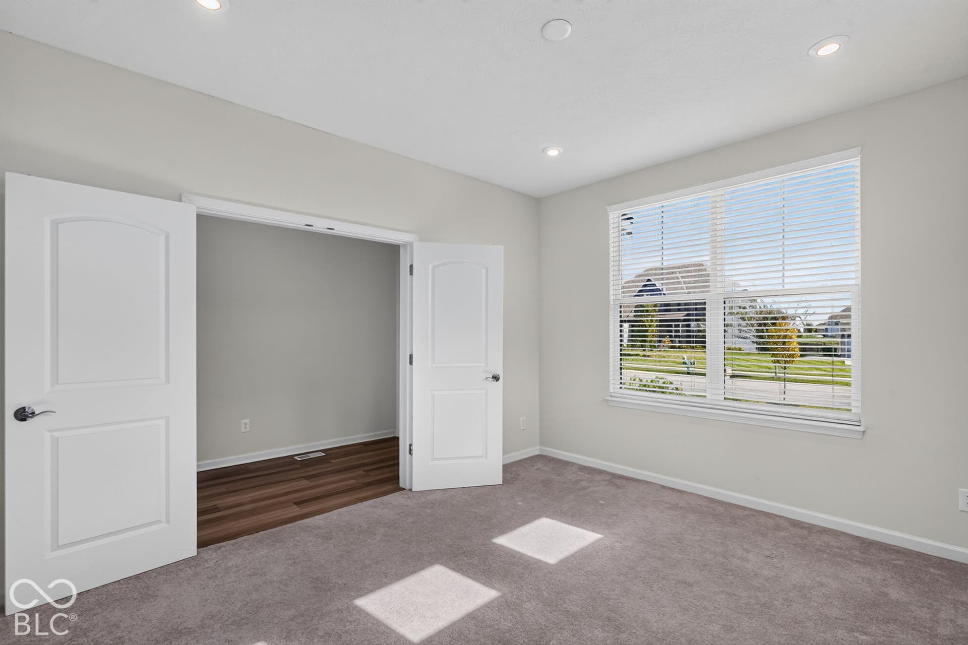 Room featuring neutral wall tones, recessed lighting, wall-to-wall carpeting, and double doors opening to a space with wood-finish flooring and a multi-pane window with installed blinds