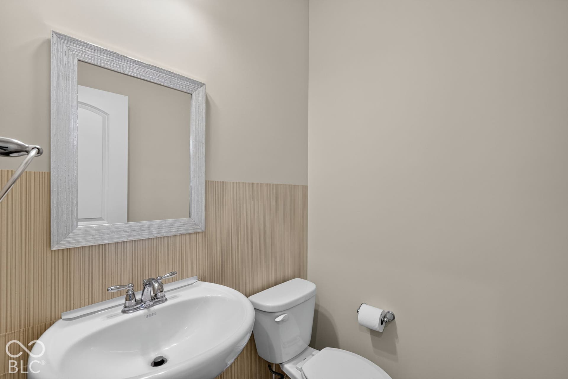 Wall-mounted white basin with a dual-handle chrome faucet, rectangular framed mirror, and vertical-texture wall treatment
