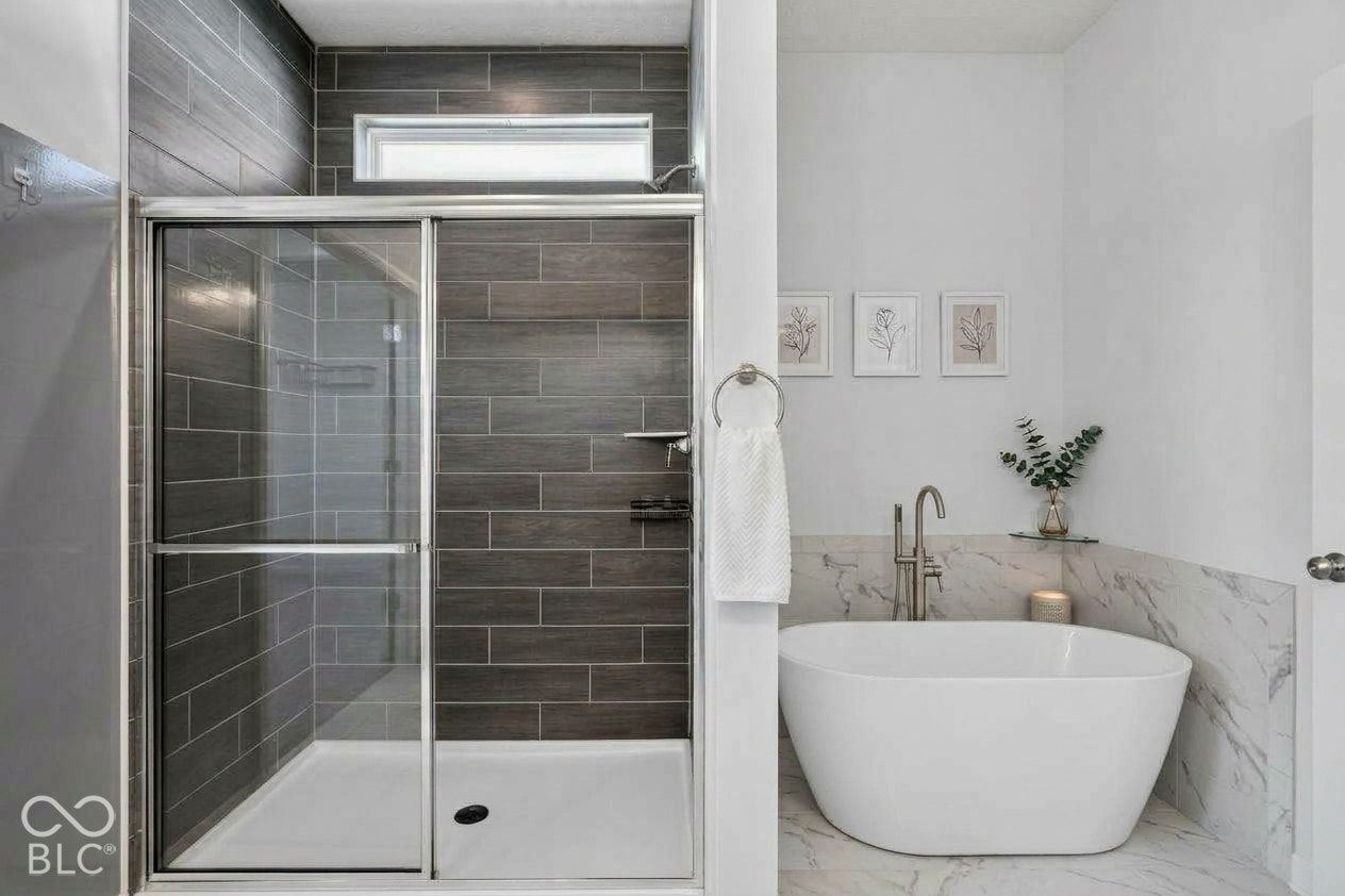 Walk-in shower with dark wood-finish tile surround and transom window, paired with a freestanding soaking tub featuring a floor-mounted faucet and stone-patterned tile wainscoting