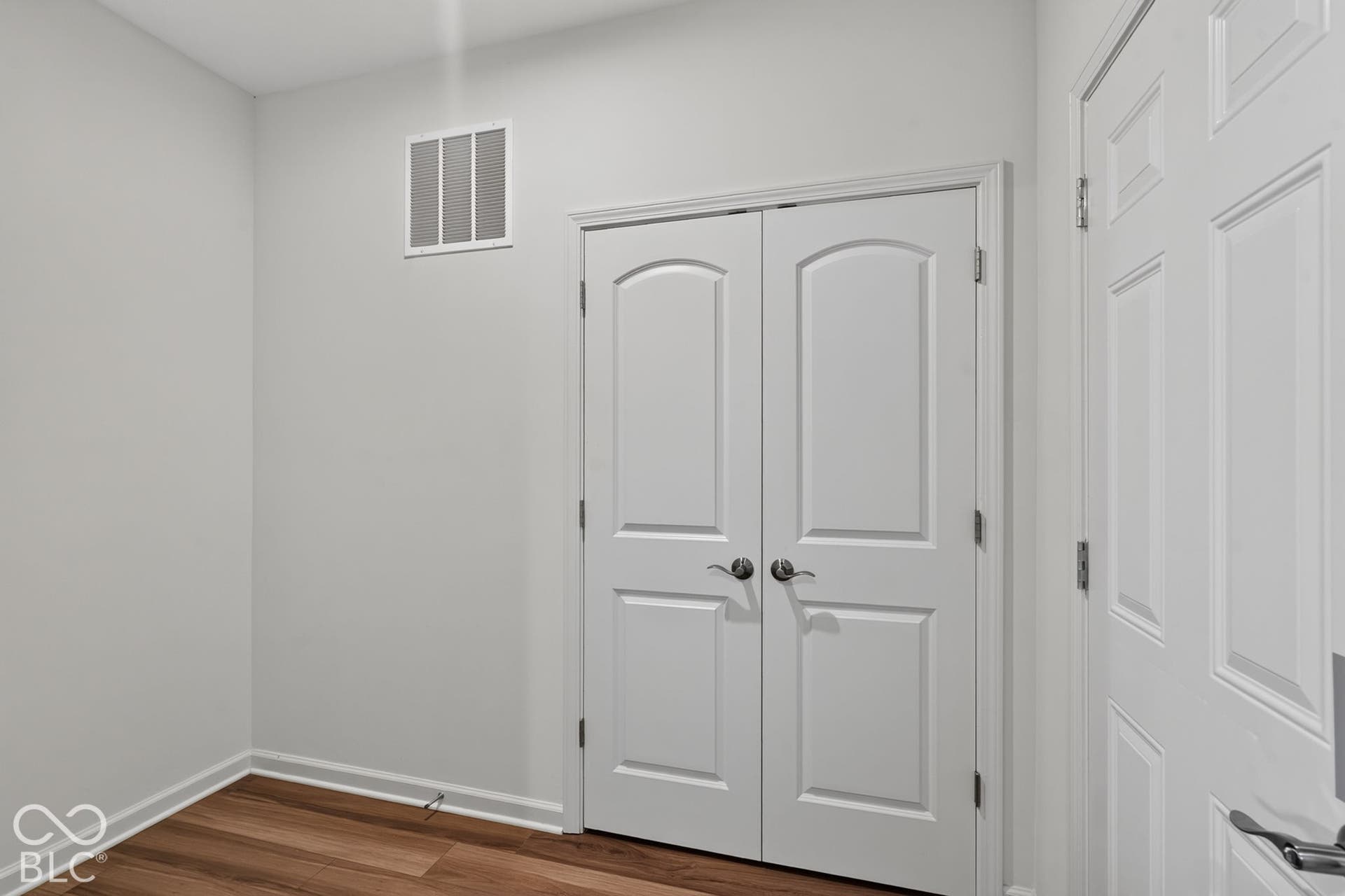 Interior space featuring wood-finish flooring and double-panel arched doors with metallic hardware