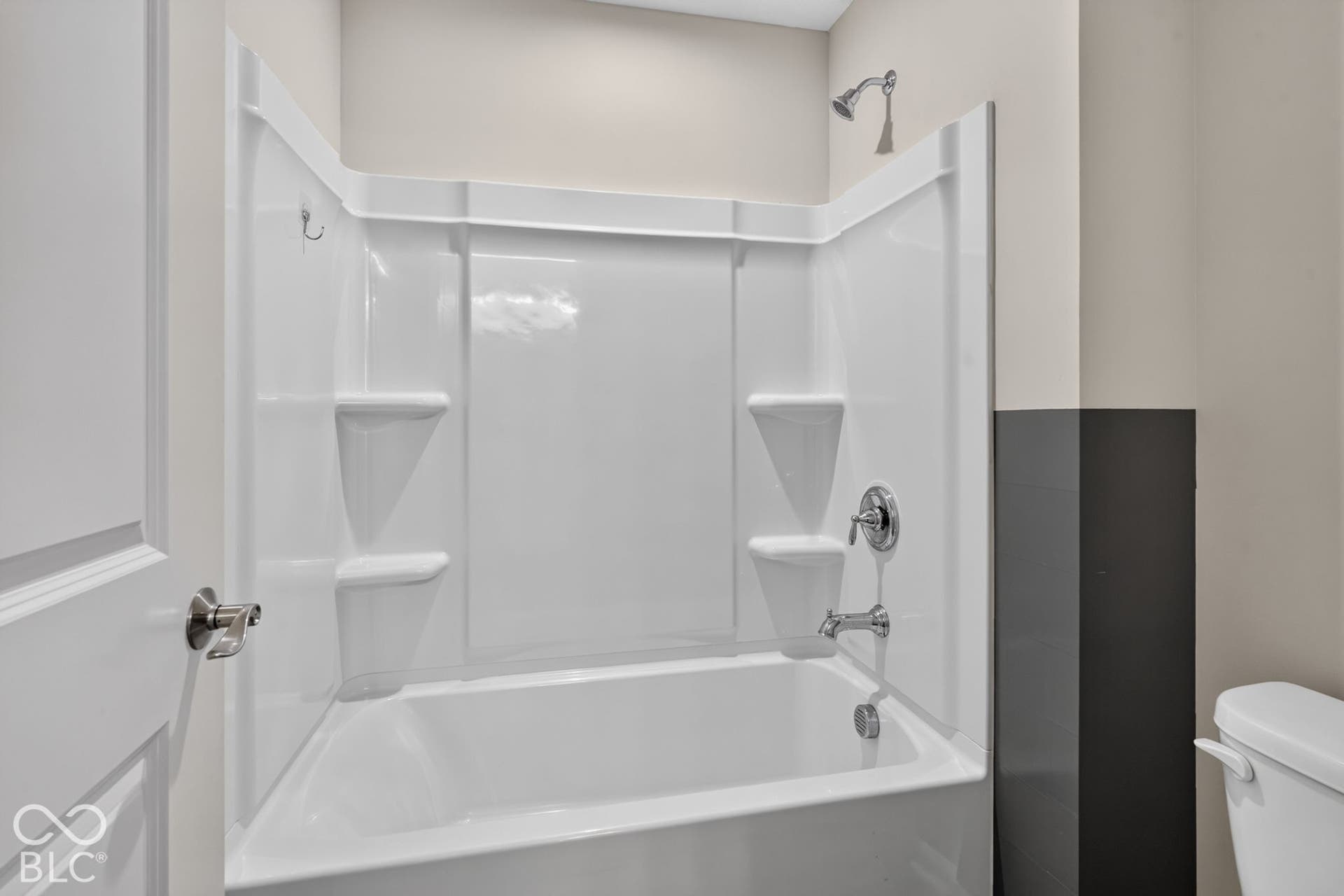 Bathtub with integrated white surround, built-in soap shelving, chrome fixtures, and a two-tone wall finish