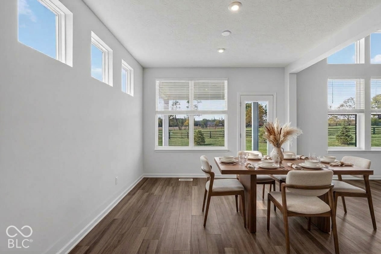 Virtually Altered - High-ceilinged room featuring wood-finish flooring, recessed lighting, expansive multi-pane windows, and a glass-paneled exterior door