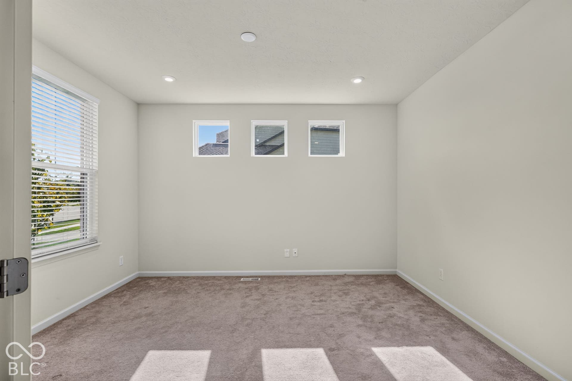 Interior space featuring neutral-toned carpeting, high-positioned square accent windows, recessed lighting, and a large side-wall window with horizontal blinds