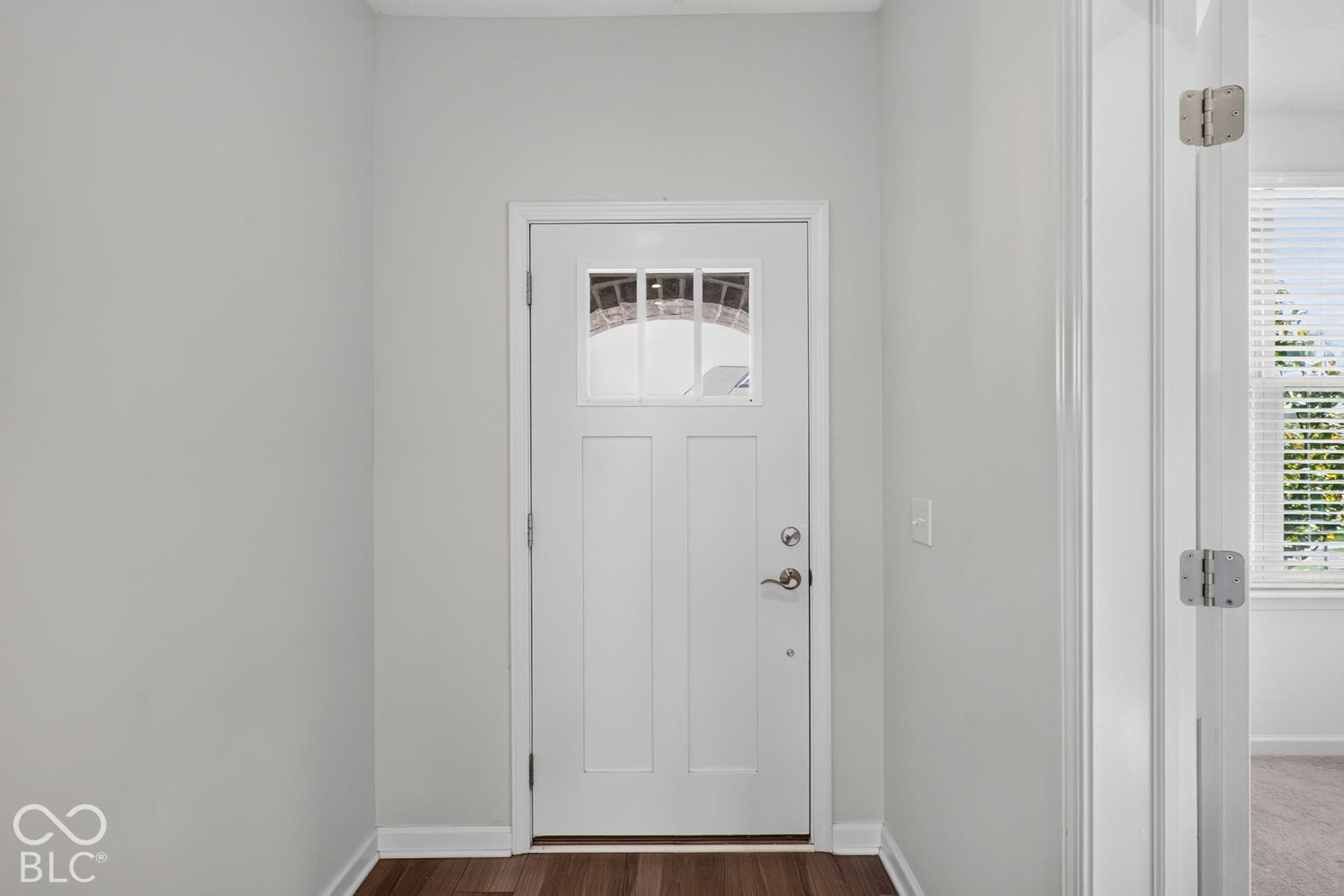 White entry door featuring a three-pane window insert, satin nickel hardware, and dark wood-finish flooring