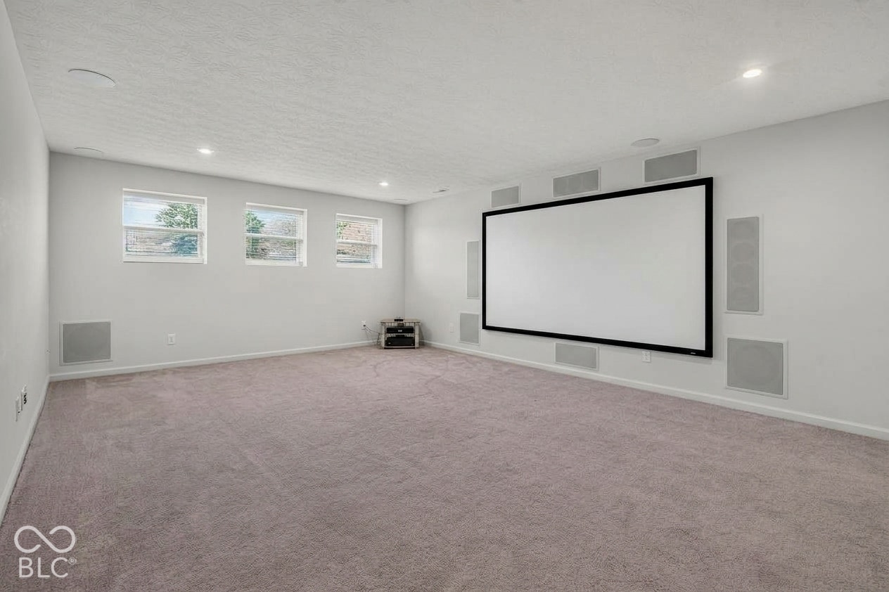 Virtually Altered - Media room featuring a wall-mounted projector screen, integrated surround sound speaker system, recessed lighting, carpeted flooring, and three windows