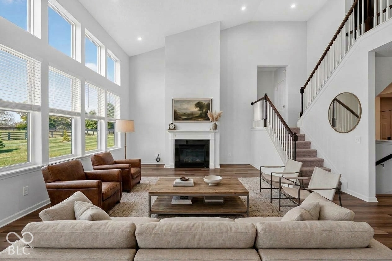 Virtually Altered - Vaulted ceilings, expansive multi-tier windows, floor-to-ceiling fireplace with a traditional mantel, and a staircase featuring a wood handrail and decorative balusters