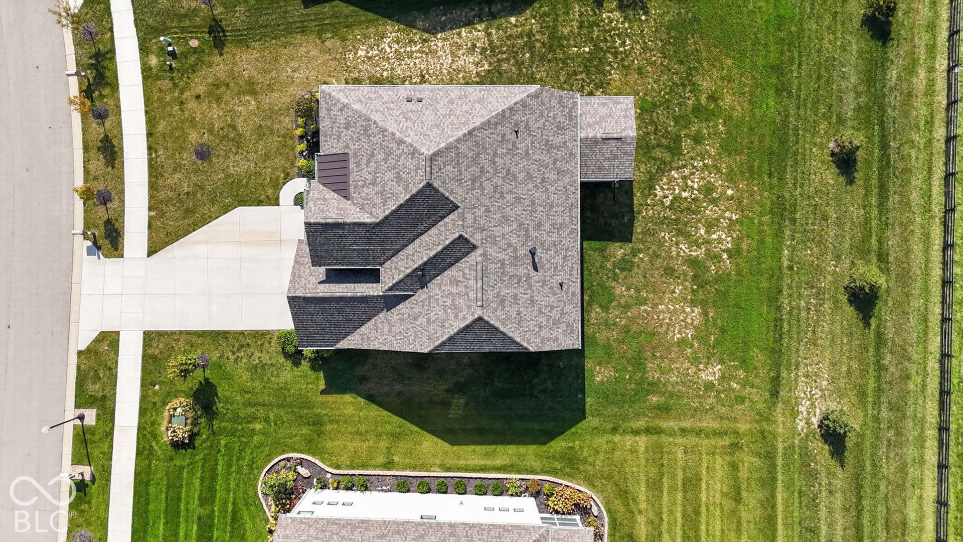 Aerial perspective featuring a multi-gabled asphalt shingle roof, concrete driveway, and expansive grass lot
