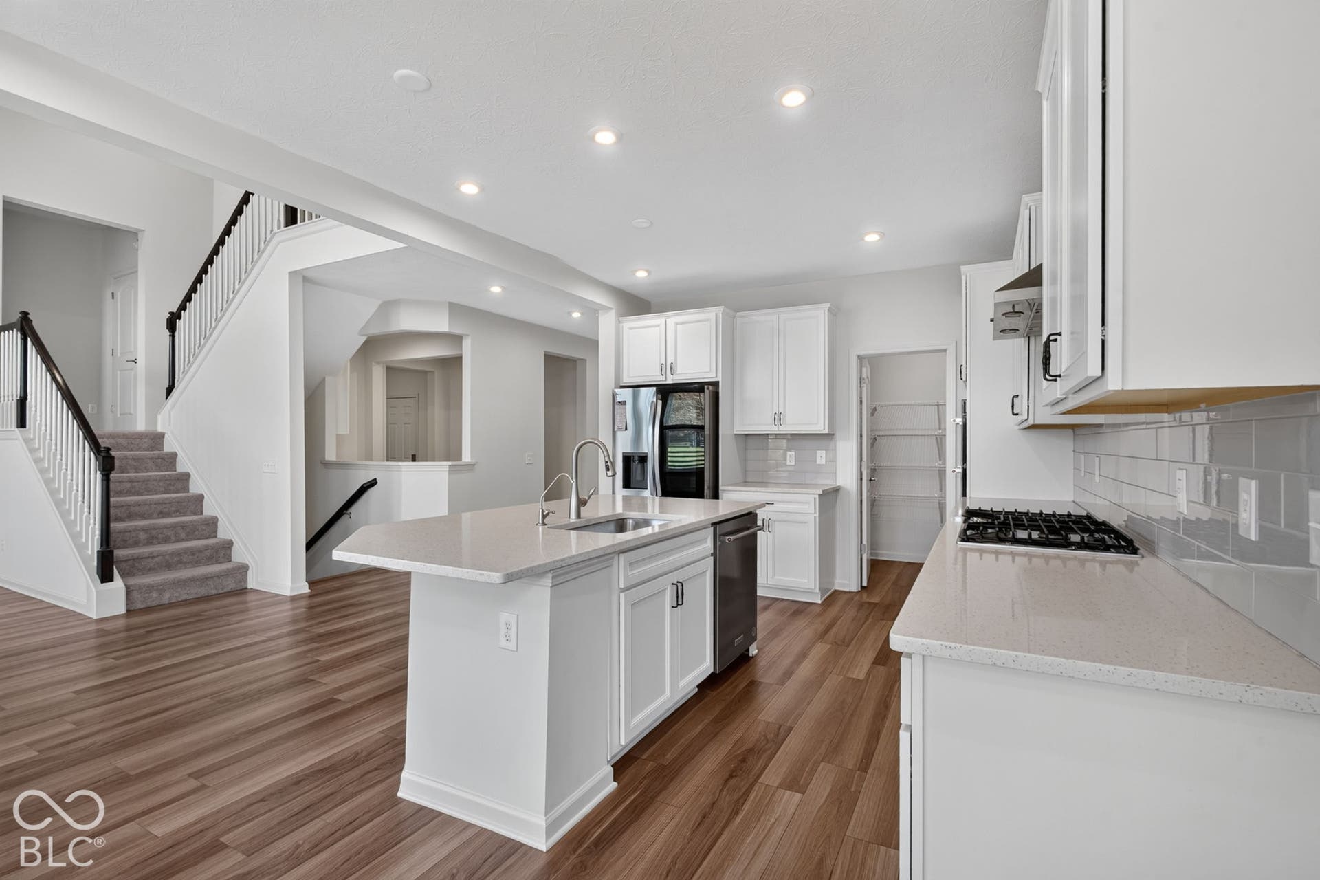 Kitchen featuring white shaker cabinetry, stone-finish countertops, subway tile backsplash, stainless steel gas cooktop, and a central island with a stainless steel sink