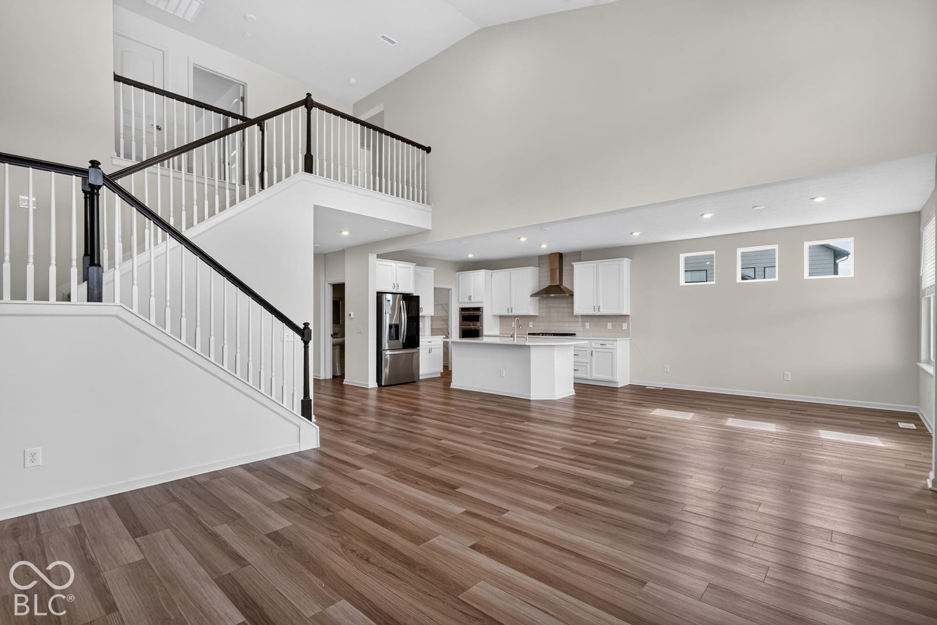 Vaulted ceilings, wood-finish flooring, staircase with a painted railing, kitchen with white cabinetry, and a central kitchen island