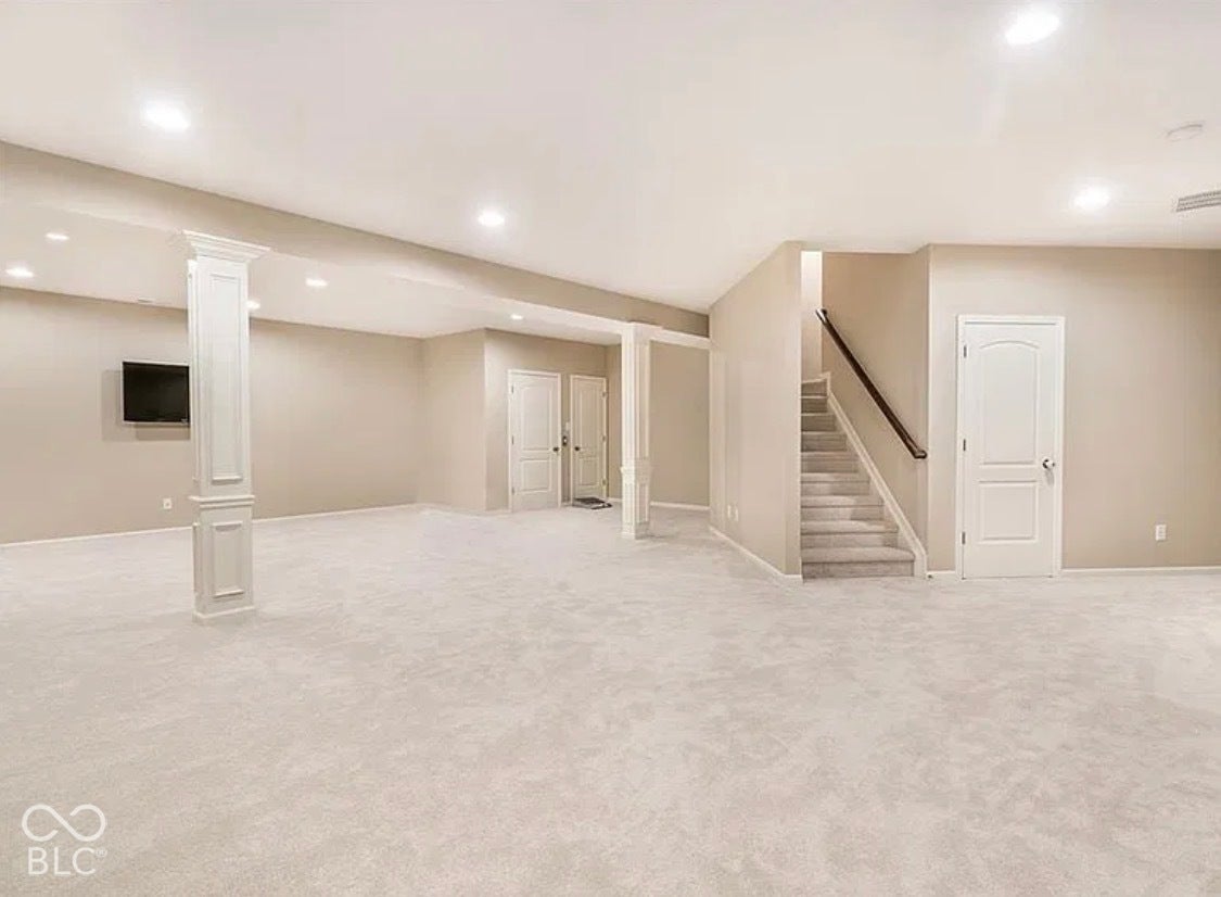 Open interior space featuring recessed ceiling lighting, structural columns with decorative molding, carpeted flooring, and a staircase with a handrail