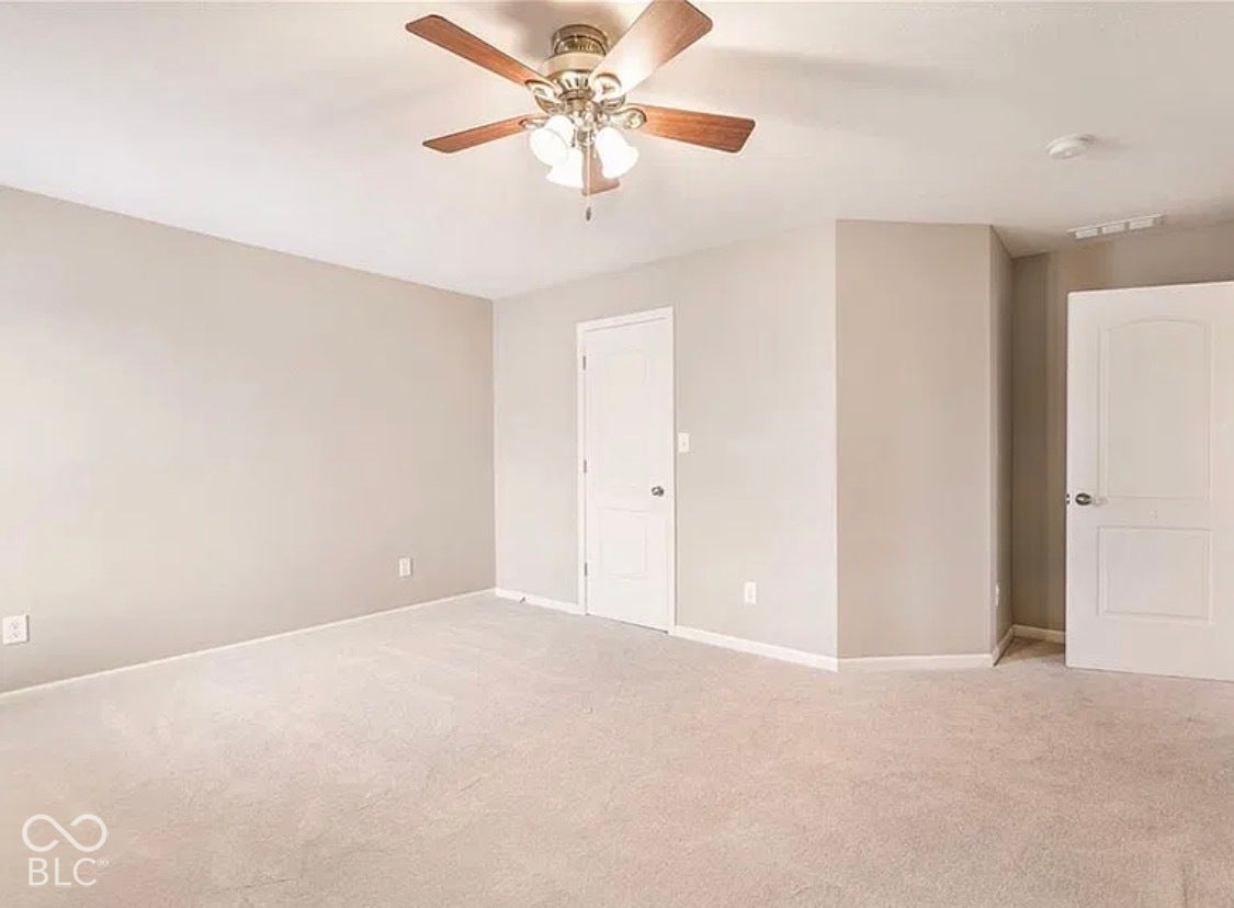 Room featuring neutral wall tones, wall-to-wall carpeting, dual six-panel interior doors, and a ceiling-mounted fan with integrated lighting