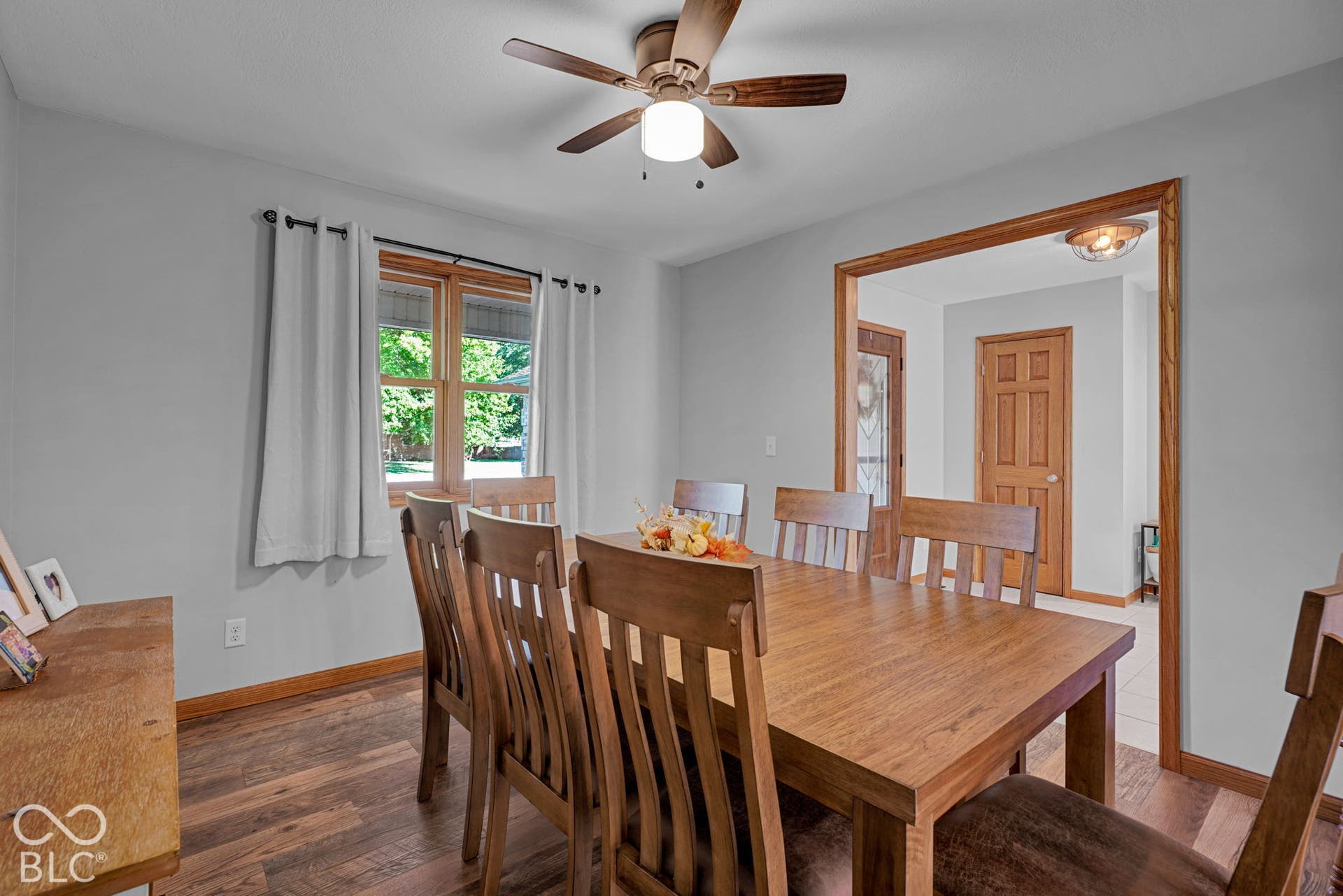 Wood-finish flooring, central ceiling fan with integrated lighting, wood-trimmed window, and stained wood-frame interior doorway