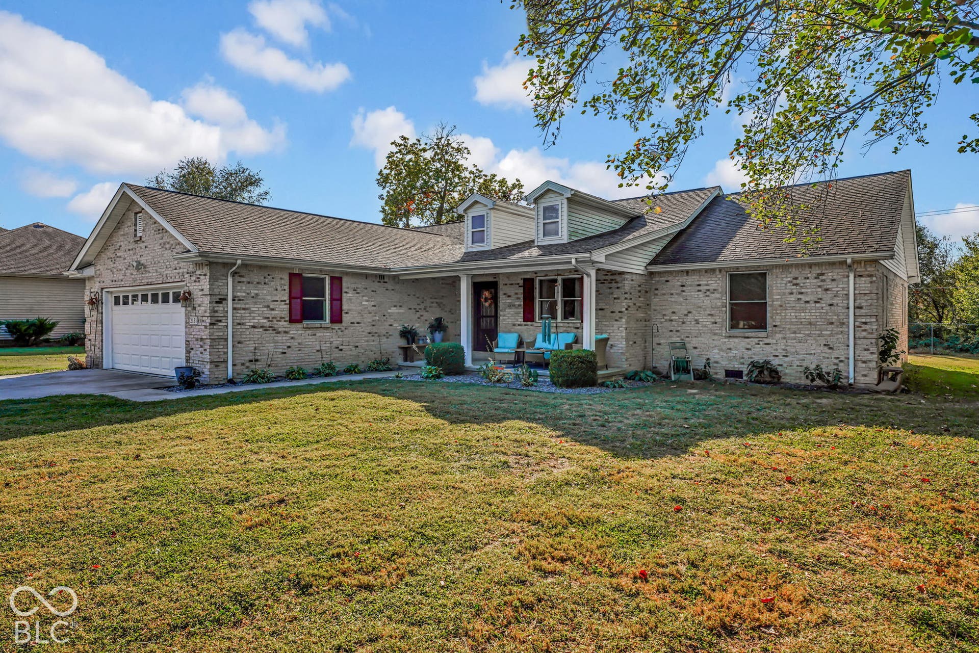 Single-story brick exterior featuring a multi-gabled roofline, dual dormer windows, attached two-car garage, and shuttered window accents