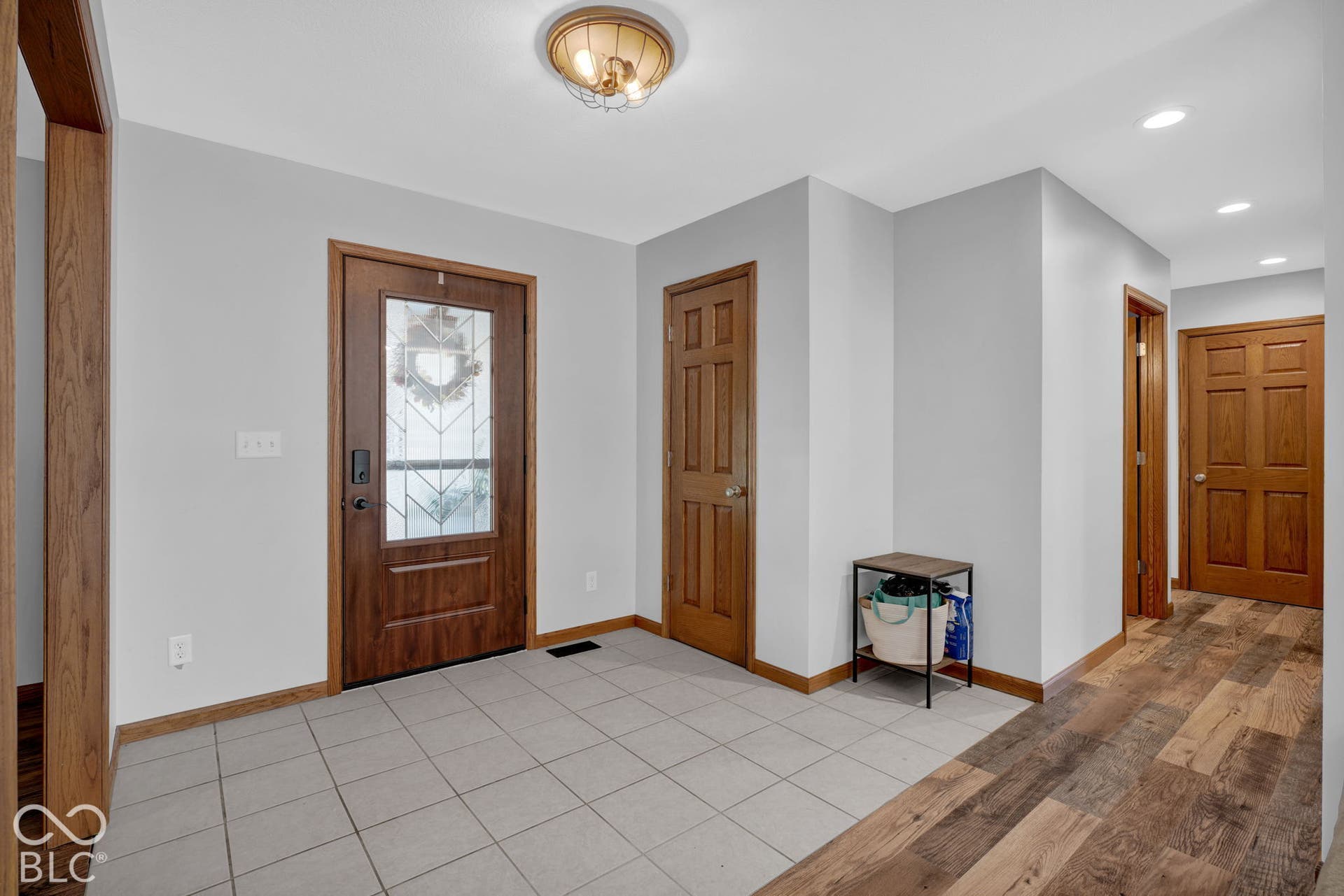 Entryway featuring neutral-toned tile flooring, wood-finish flooring, a wood-frame front door with decorative glass inlay, six-panel wood doors, and a decorative flush-mount ceiling fixture