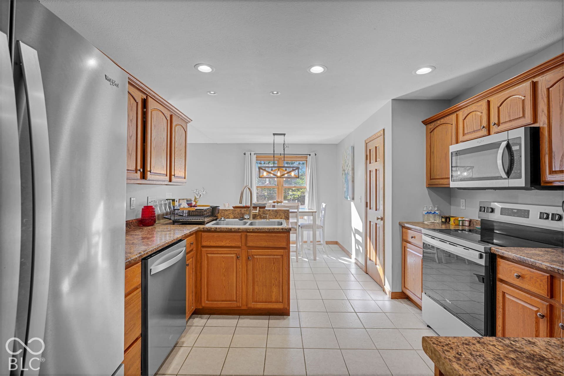 Kitchen featuring wood cabinetry, stone-patterned laminate countertops, stainless steel appliances, ceramic tile flooring, and recessed ceiling lighting