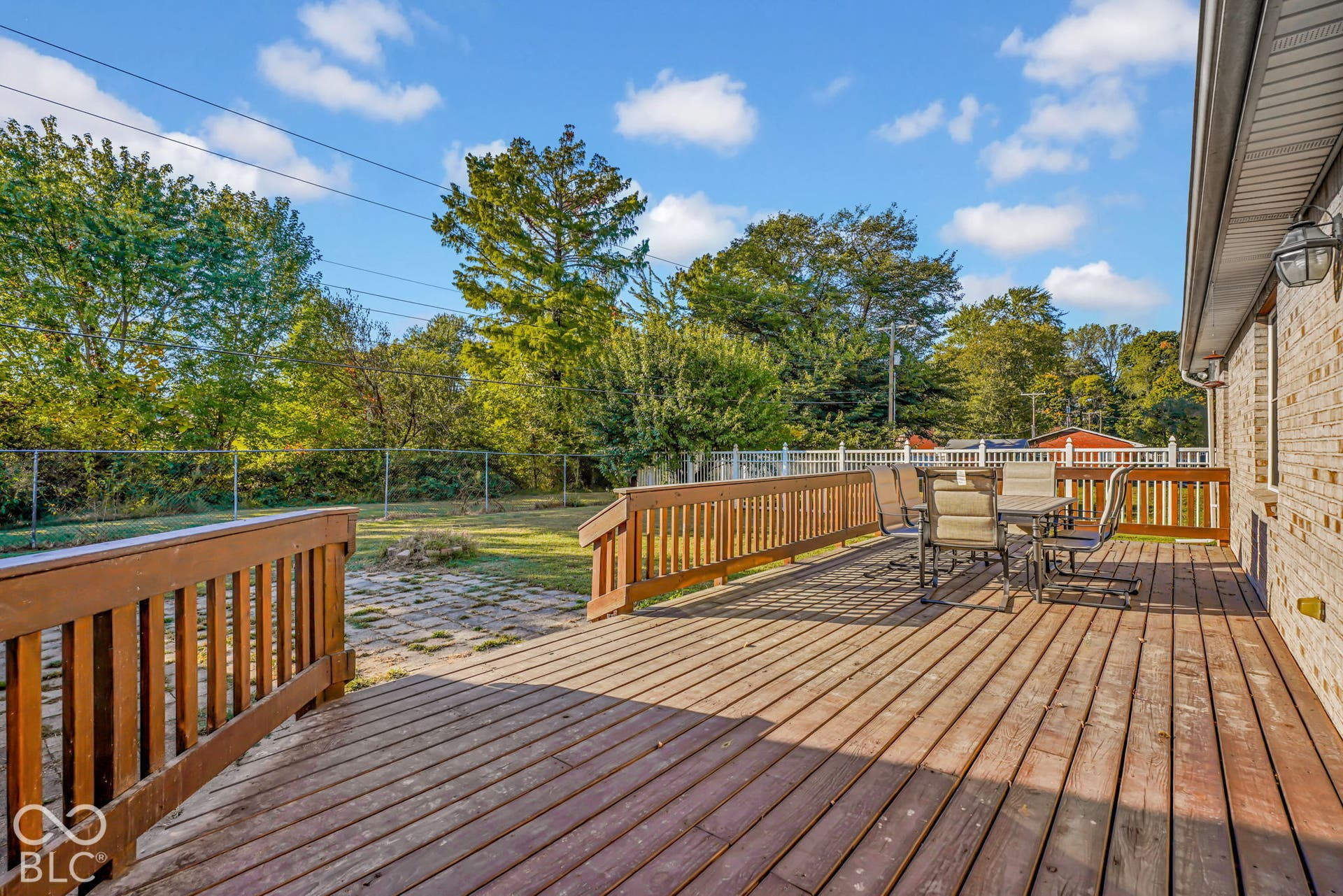 Elevated wood deck featuring a balustrade railing, stone paver patio area, and a fenced backyard