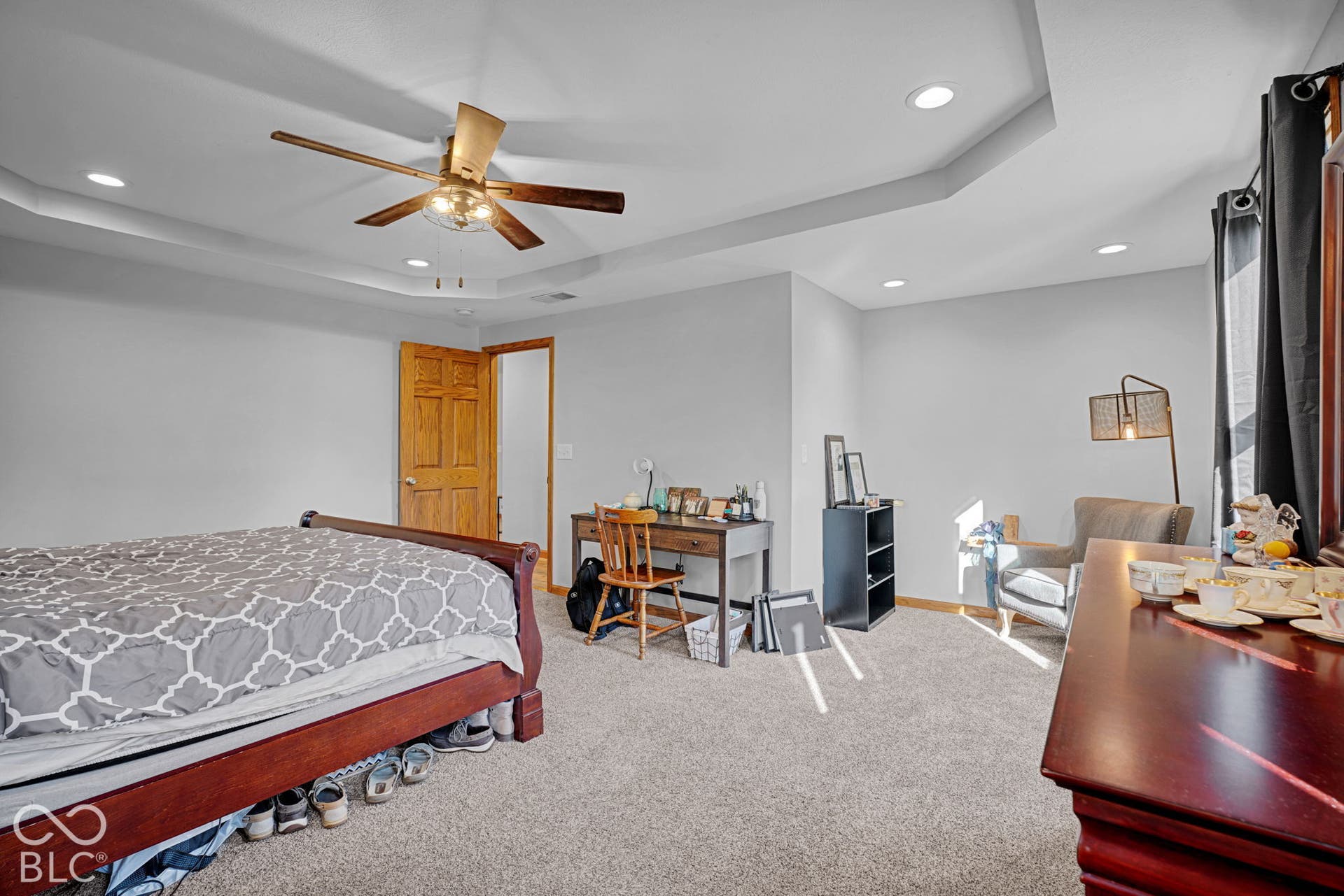 Tray ceiling featuring recessed lighting and a central ceiling fan, paired with neutral carpeting and a natural wood-finish interior door
