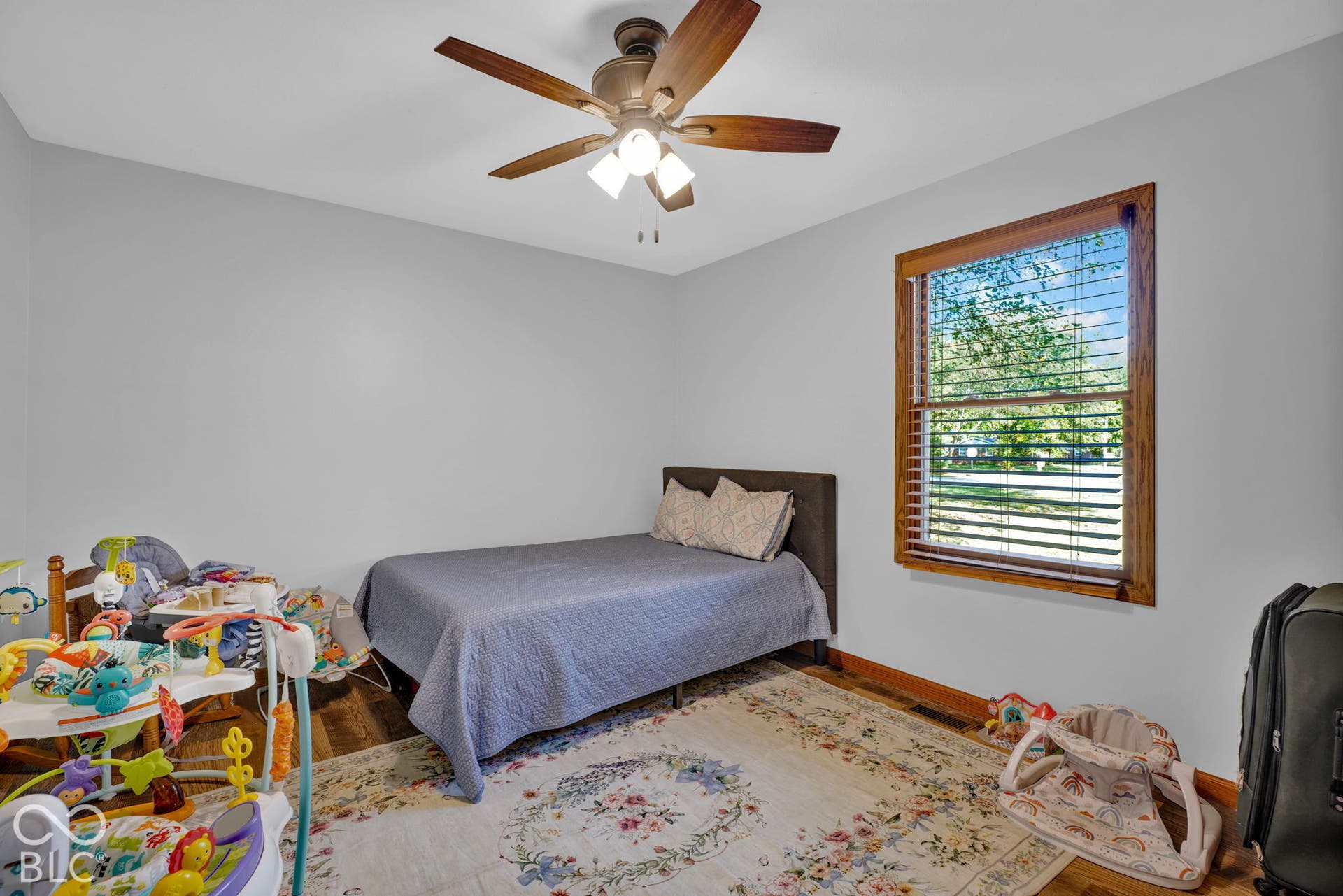 Room featuring wood-finish flooring, a wood-framed window with integrated blinds, and a ceiling fan with integrated lighting