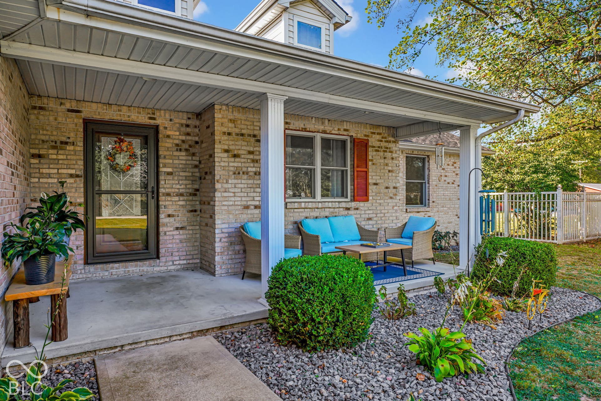 Brick exterior featuring a covered front porch, structural columns, shutter accents, and a low-maintenance stone landscaping bed