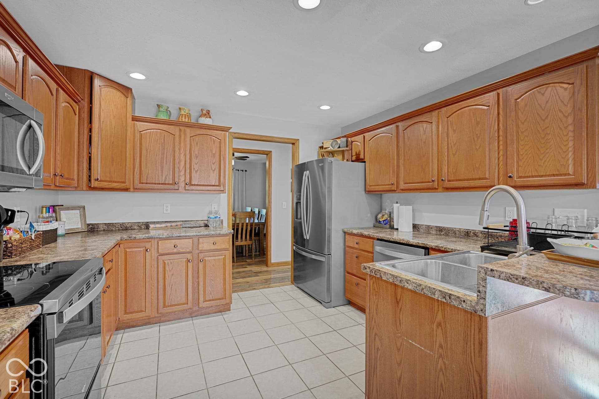 Kitchen featuring wood cabinetry, stone-finish countertops, stainless steel appliances, dual-basin sink with gooseneck faucet, and recessed lighting